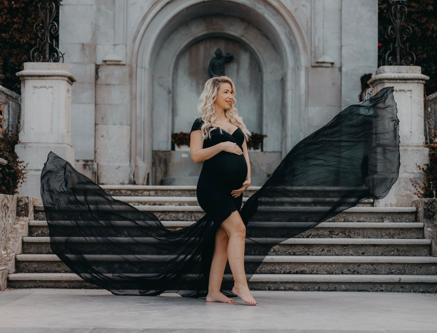 Dramatic maternity photo on stone steps with flowing black fabric.