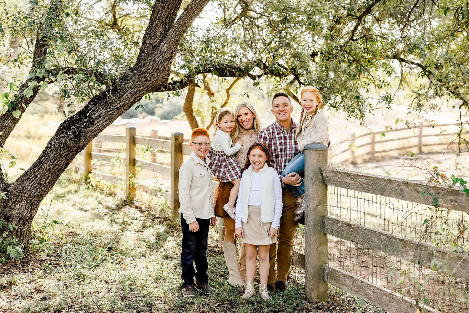 Family of six posing under a large oak tree near a wooden fence at a mini session in Bee Cave, Tx  by Shannon Worley Photography.