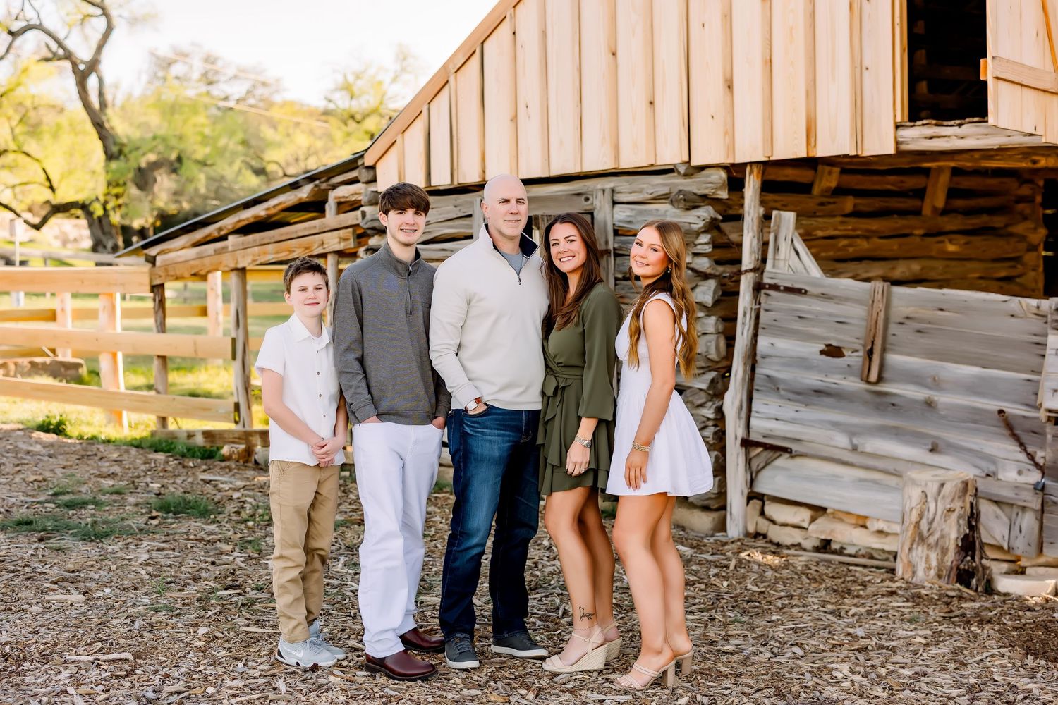 Family of five posing in front of a rustic log cabin outdoors at a mini session in Commons Ford Ranch in Bee Cave, Tx by Shannon Worley.