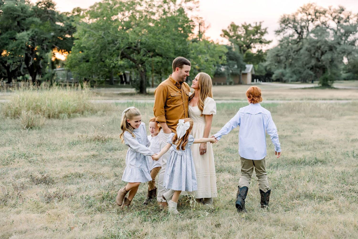 Family of six sharing a joyful moment in sunlit meadow surrounded by tall trees at a mini session by Shannon Worley photography in Dripping