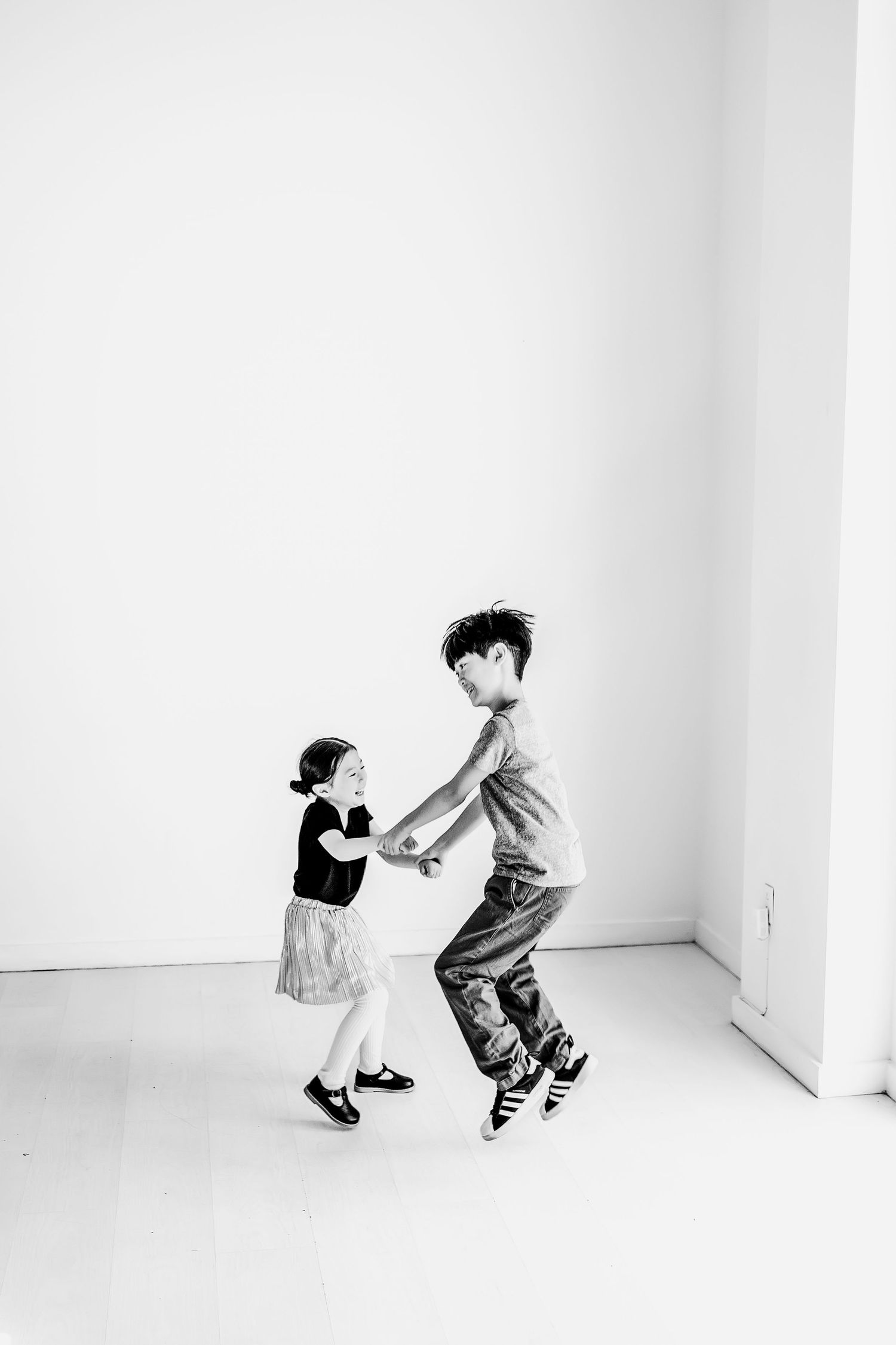 Two children dancing and playing together in a bright white room, captured in black and white photography at Lumen Studio In Austin, Tx
