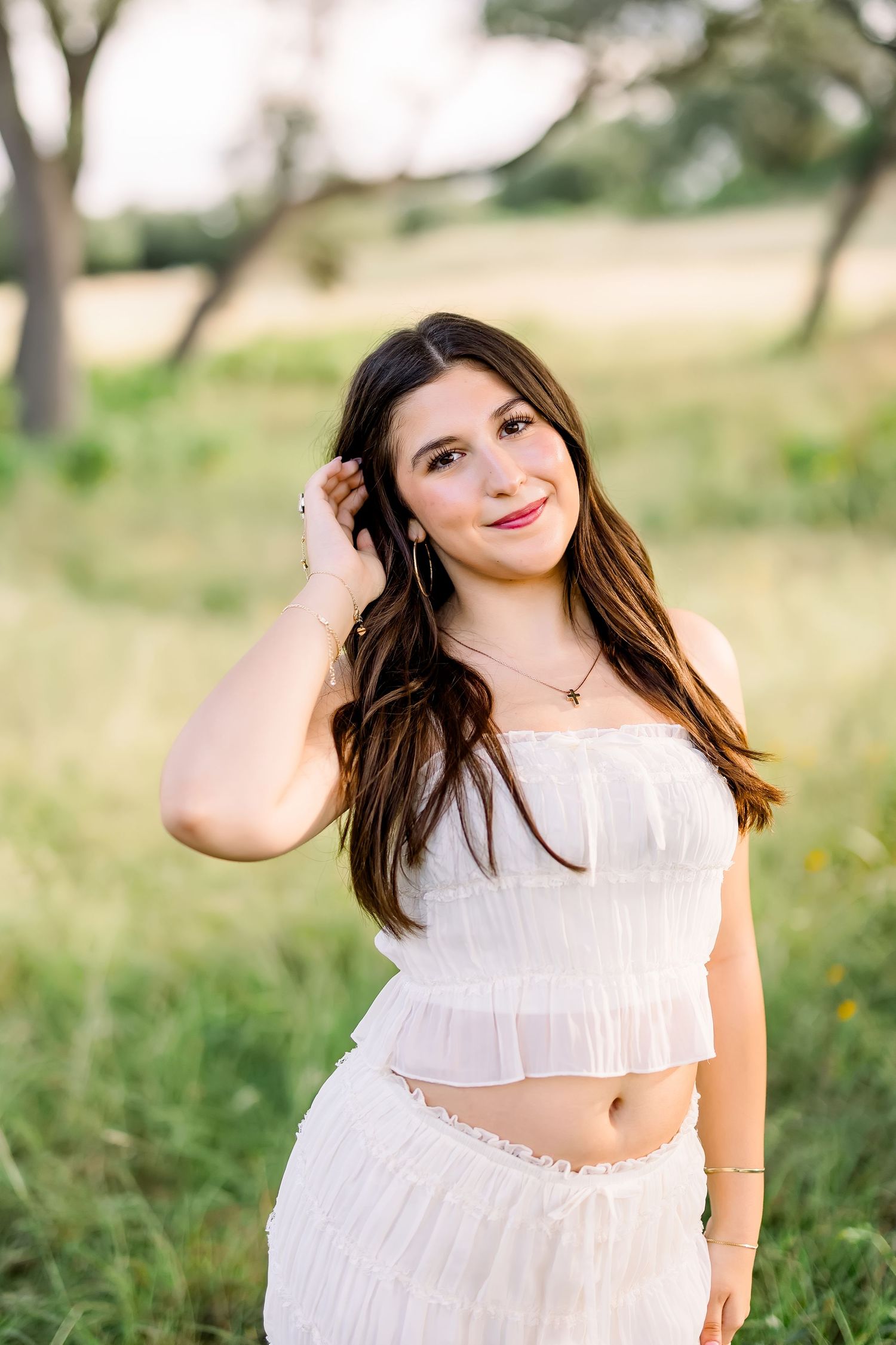 A smiling brunette young woman in a white crop top and skirt poses in a golden sunlit field.