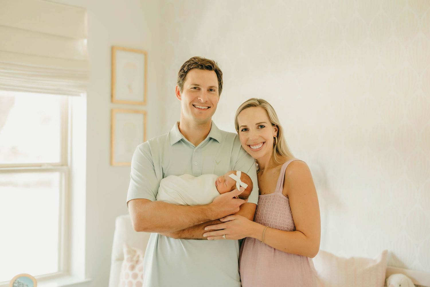 Smiling couple holding newborn baby in bright white nursery room.
