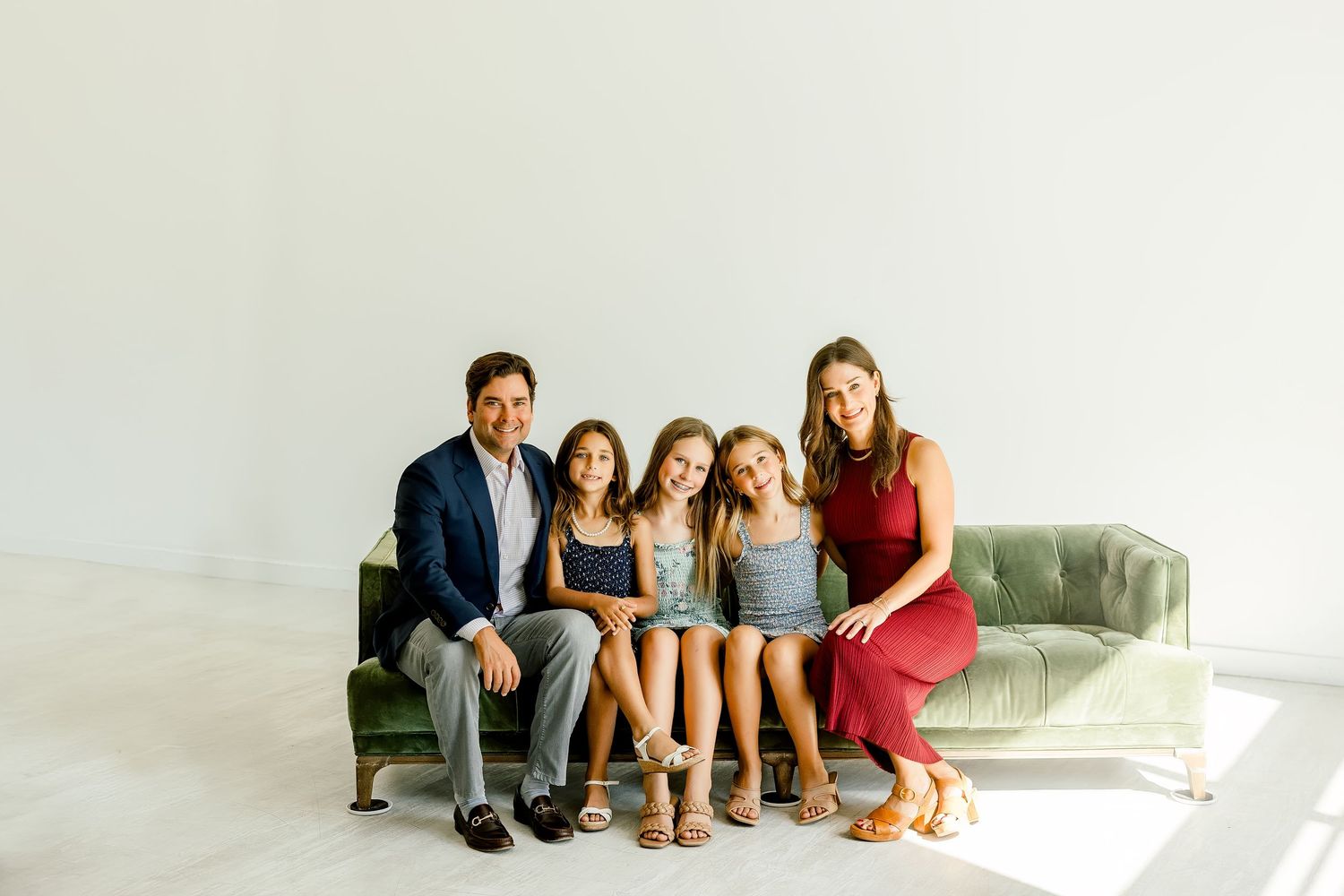 Happy family of five posing together on a green velvet couch in a bright white studio at a mini session located Lumen Studio in Austin, TX