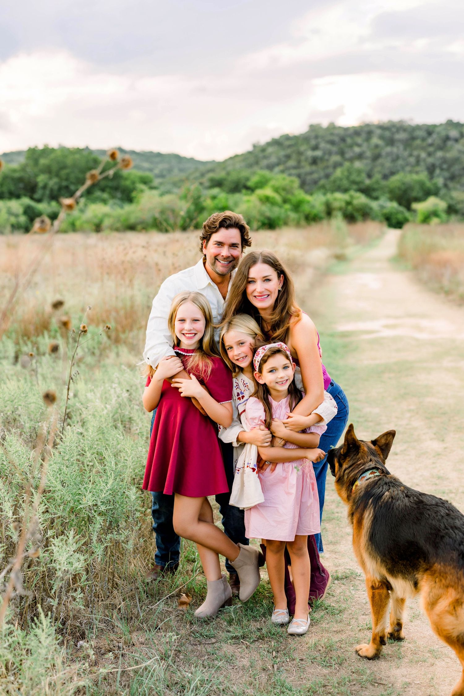 Family of five with a German Shepherd dog posing on a scenic trail at a mini session in Commons Ford Ranch in Bee Cave, Tx.