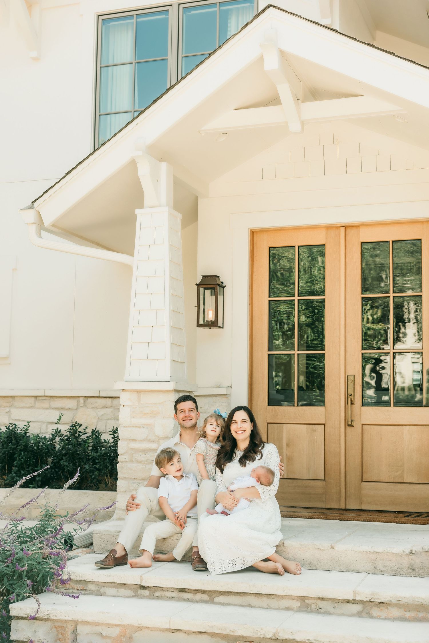 A young family with three children poses on the front steps of their elegant home.