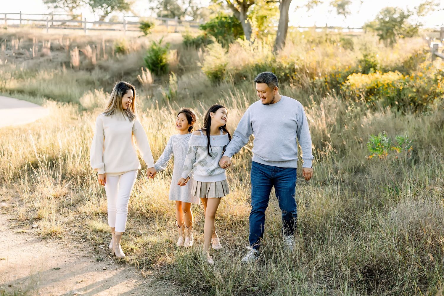 Family of four holding hands while walking along a sunlit nature path at a mini session in Bee Cave, Tx by Shannon Worley Photography.