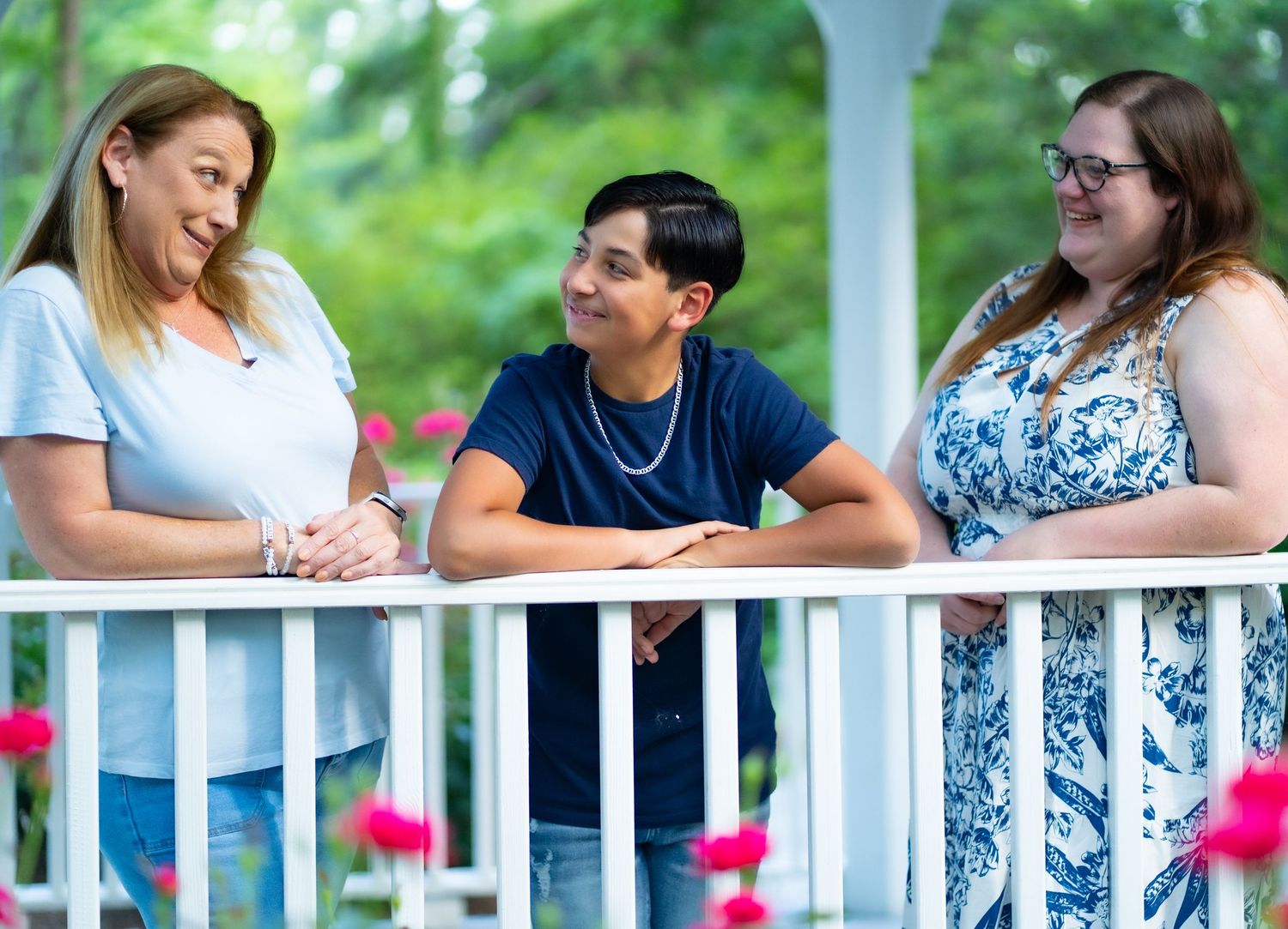 Students sit together and collaborate at an outdoor white porch railing with lush green foliage in the background.