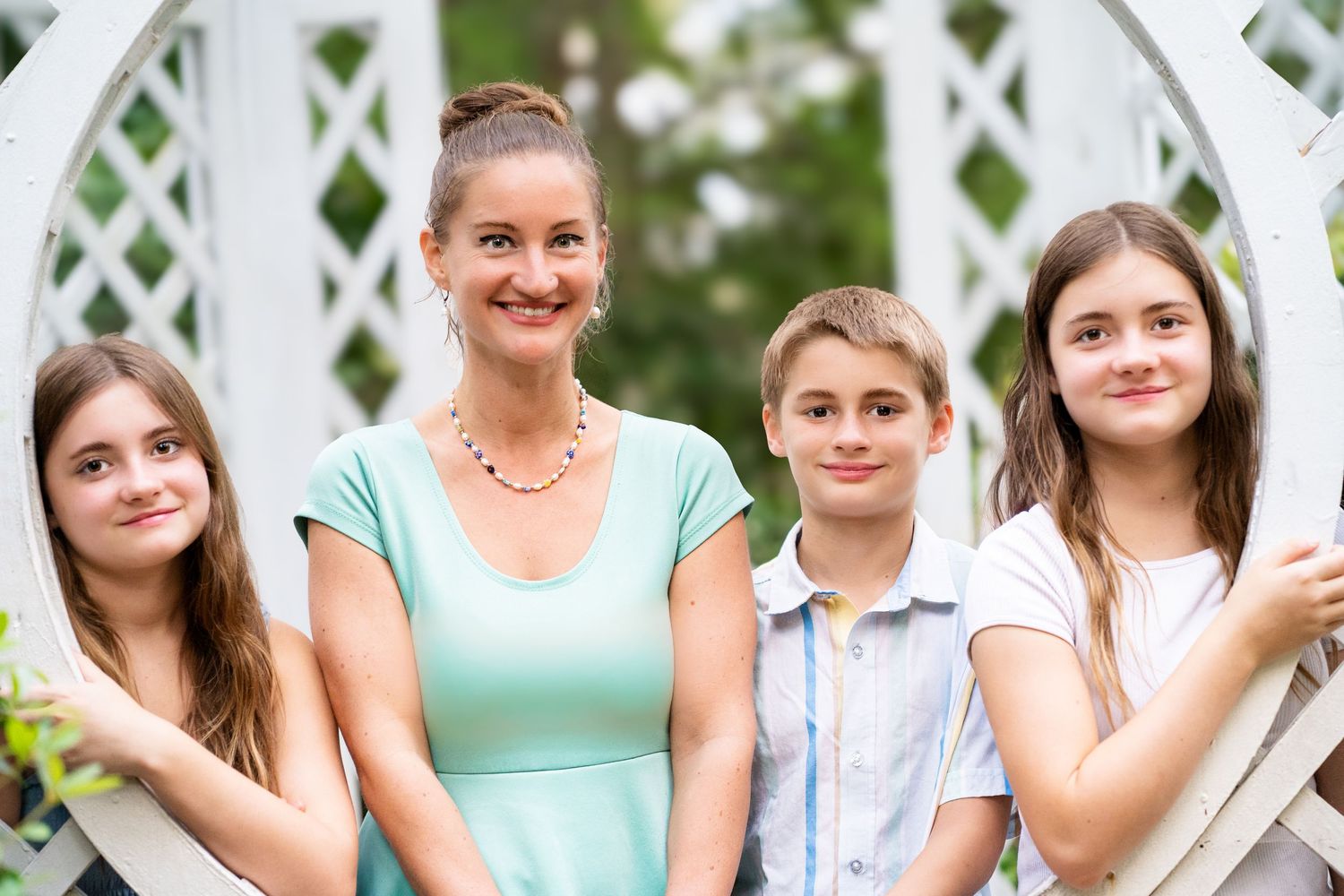 A group of people in summer attire pose together on white lattice steps in an outdoor garden setting.