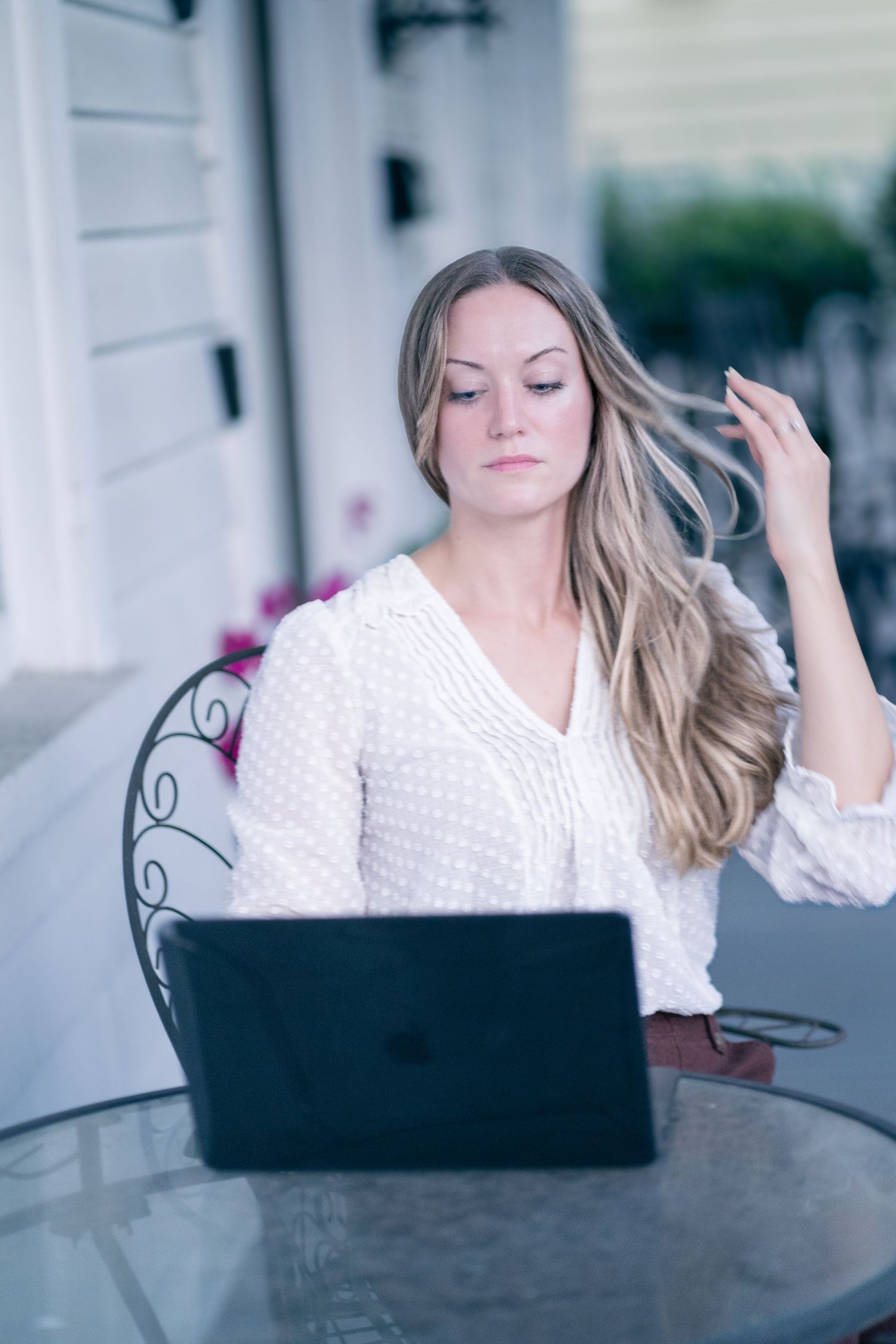 Person working on laptop while sitting at outdoor patio table with decorative railings.