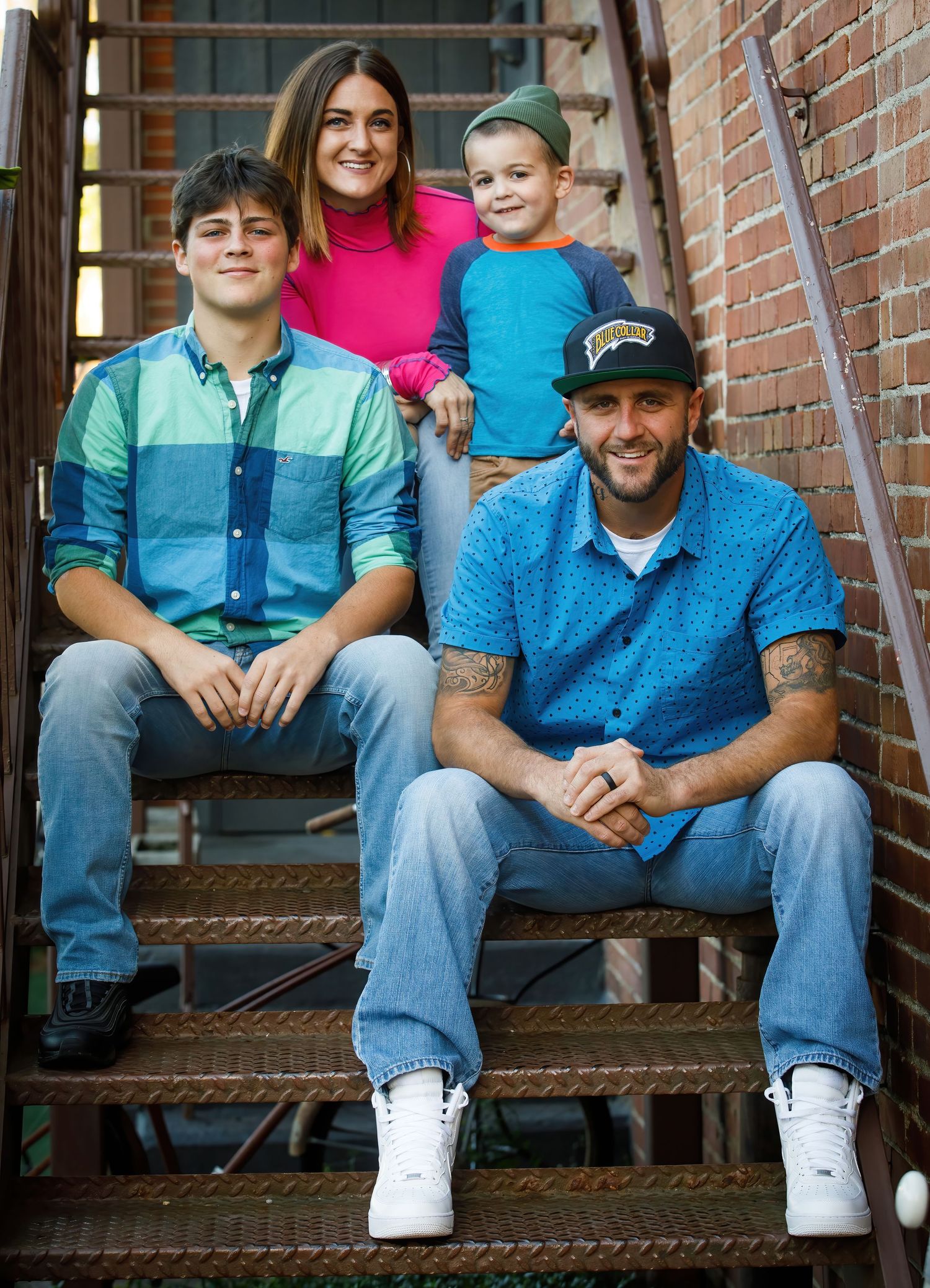 Casual family sitting together on brick steps in matching blue outfits during an outdoor photo session.