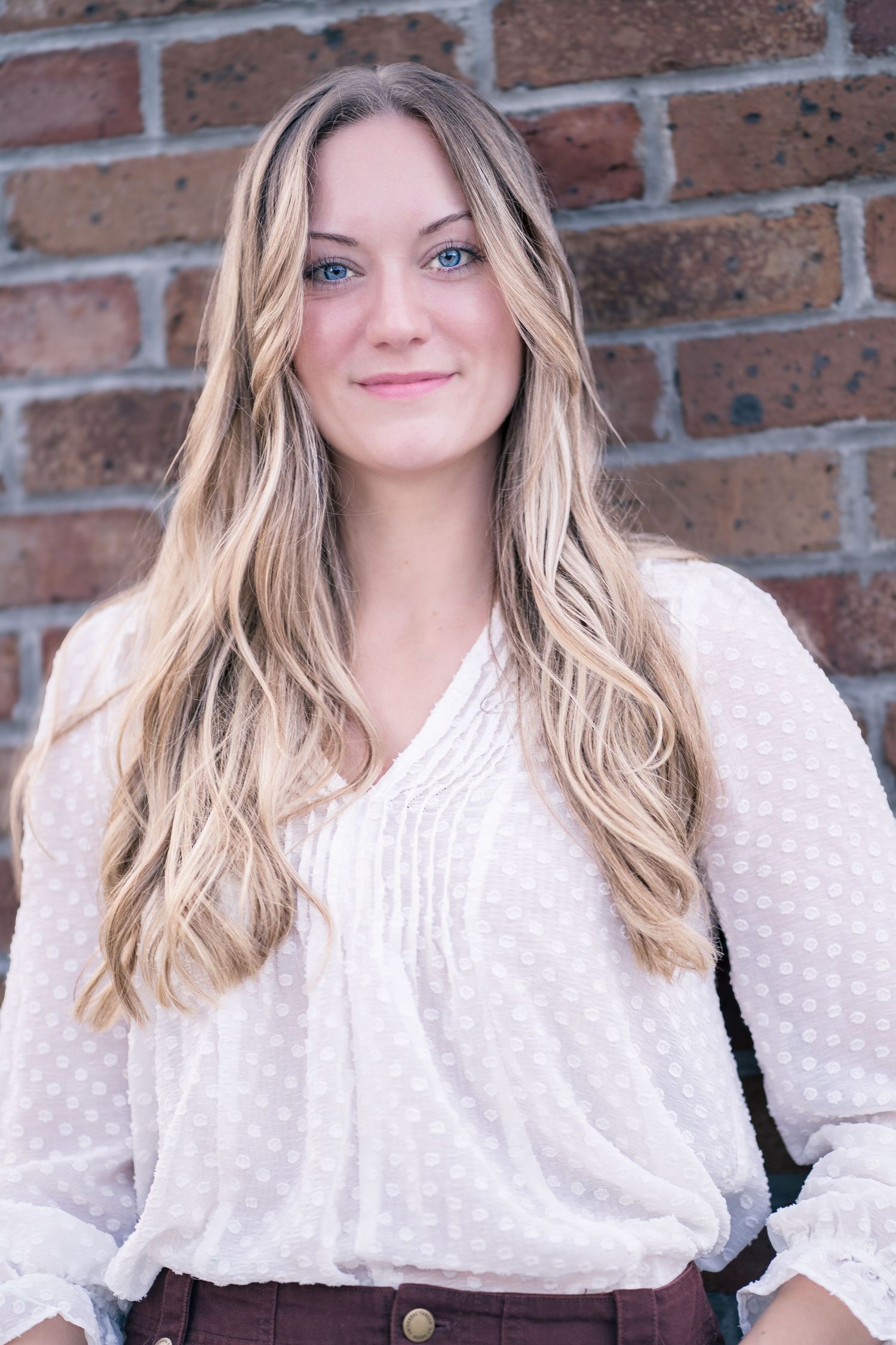 Portrait against rustic brick wall wearing white textured blouse with flowing sleeves.
