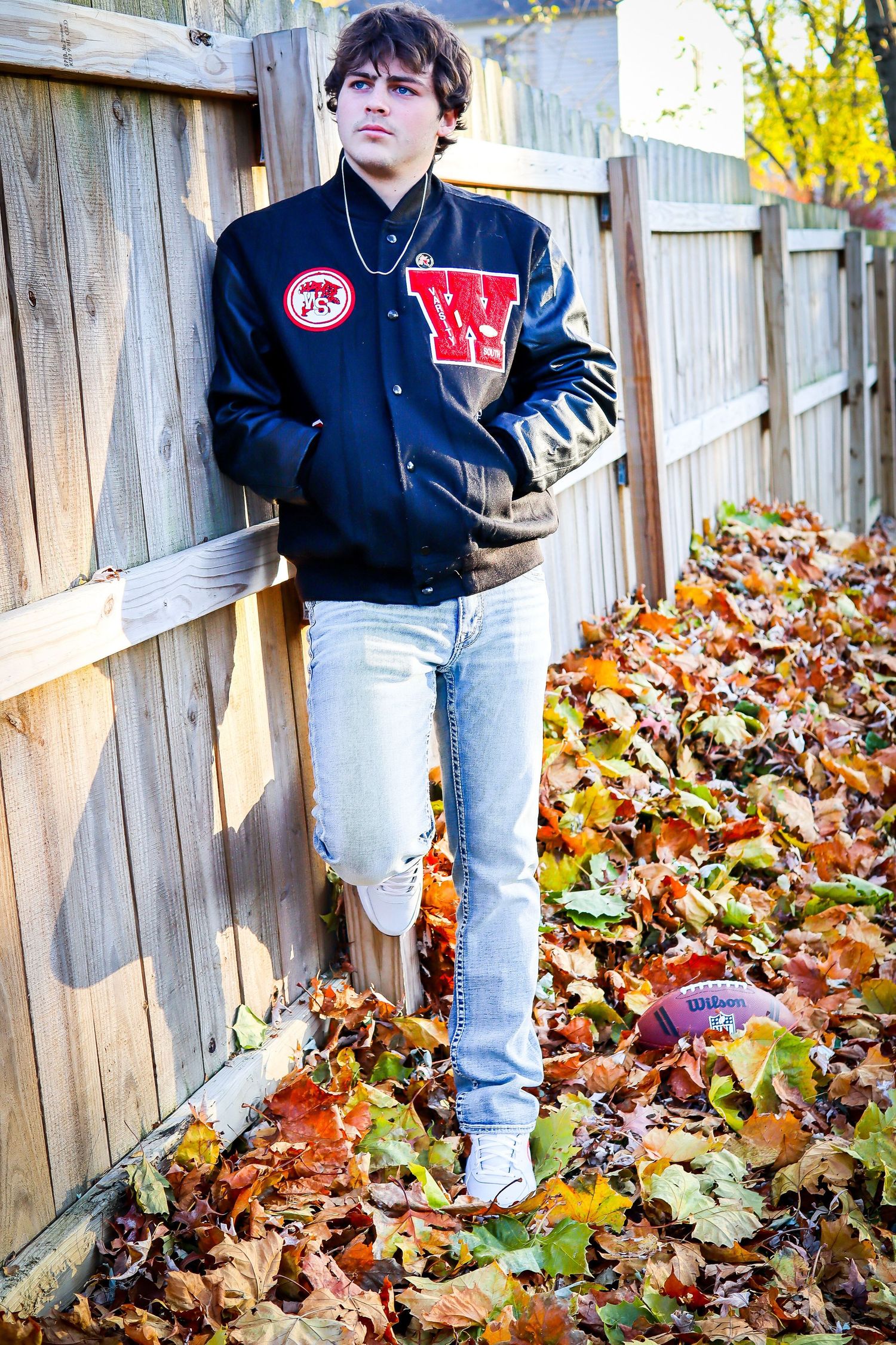 Autumn scene with fallen leaves against wooden fence and navy jacket.