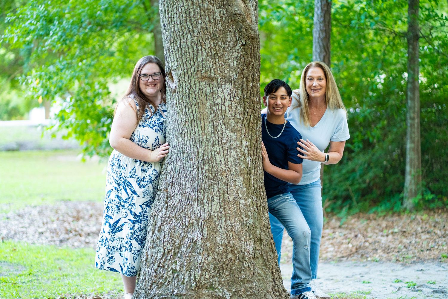 People gather around a large tree trunk in a green park setting for outdoor portraits.
