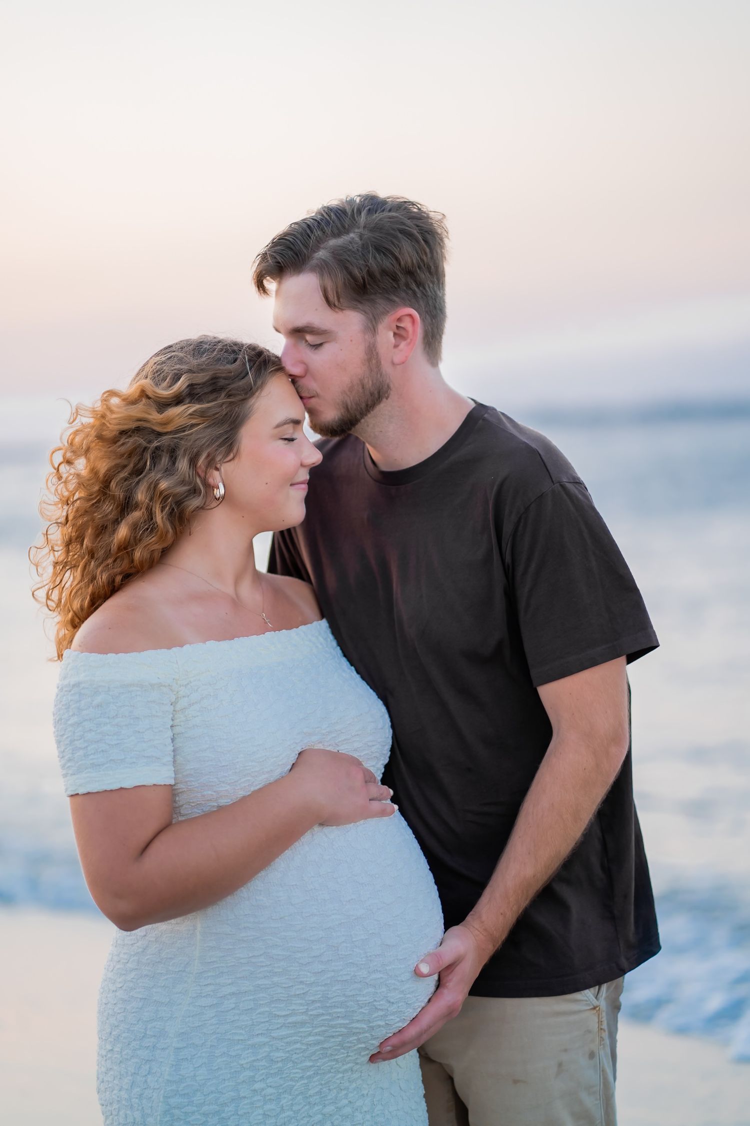 A couple shares romantic moments on the beach at sunset in a series of intimate poses against the ocean backdrop.
