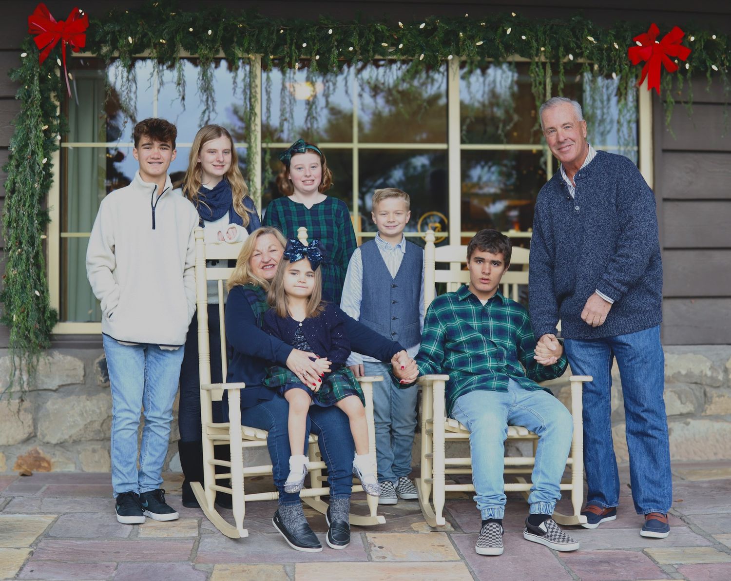 Holiday family portrait on porch with red bows and wooden rocking chairs.