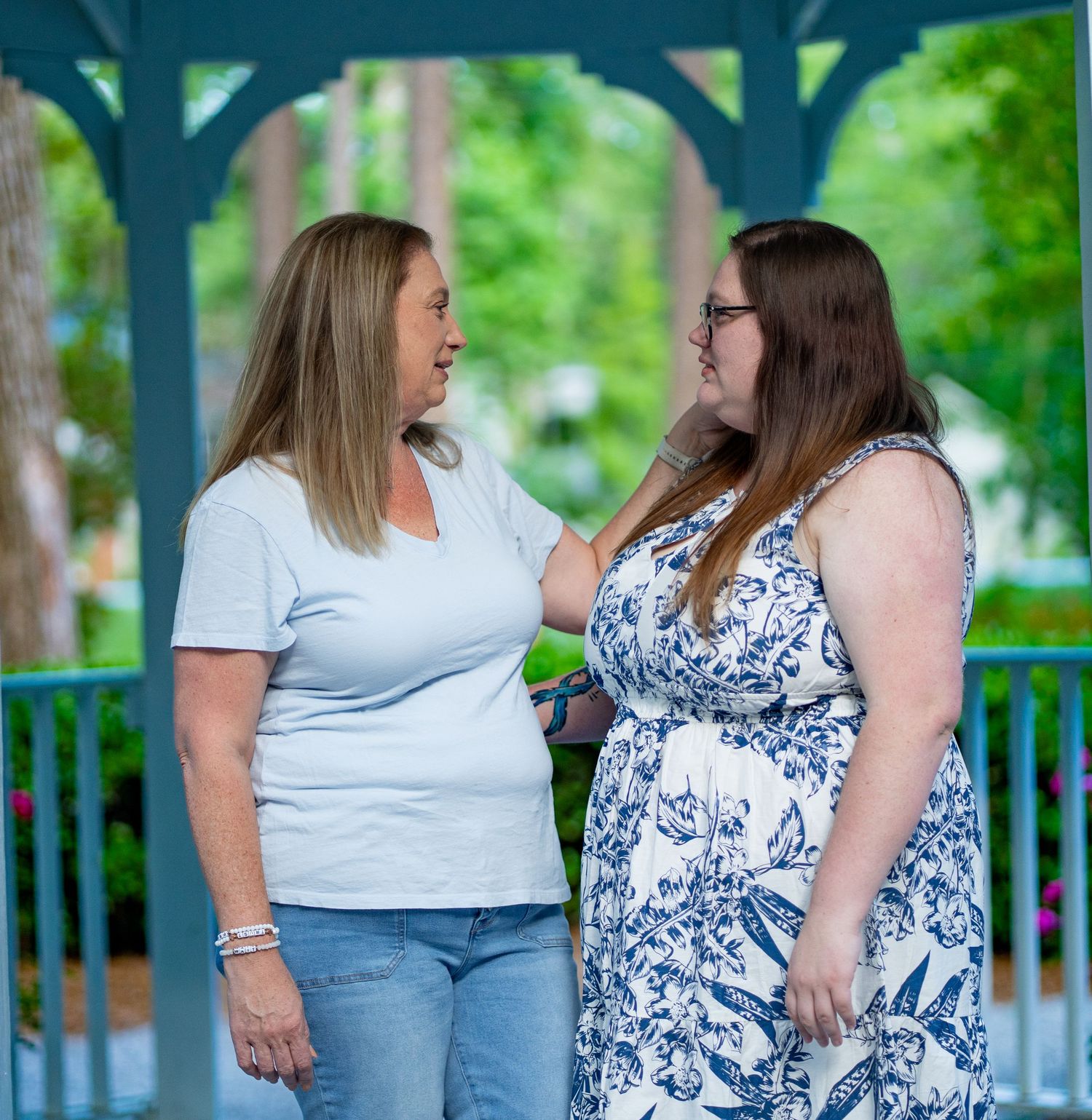 Two women in casual attire sharing a heartfelt conversation while standing outdoors on a green wooden deck.