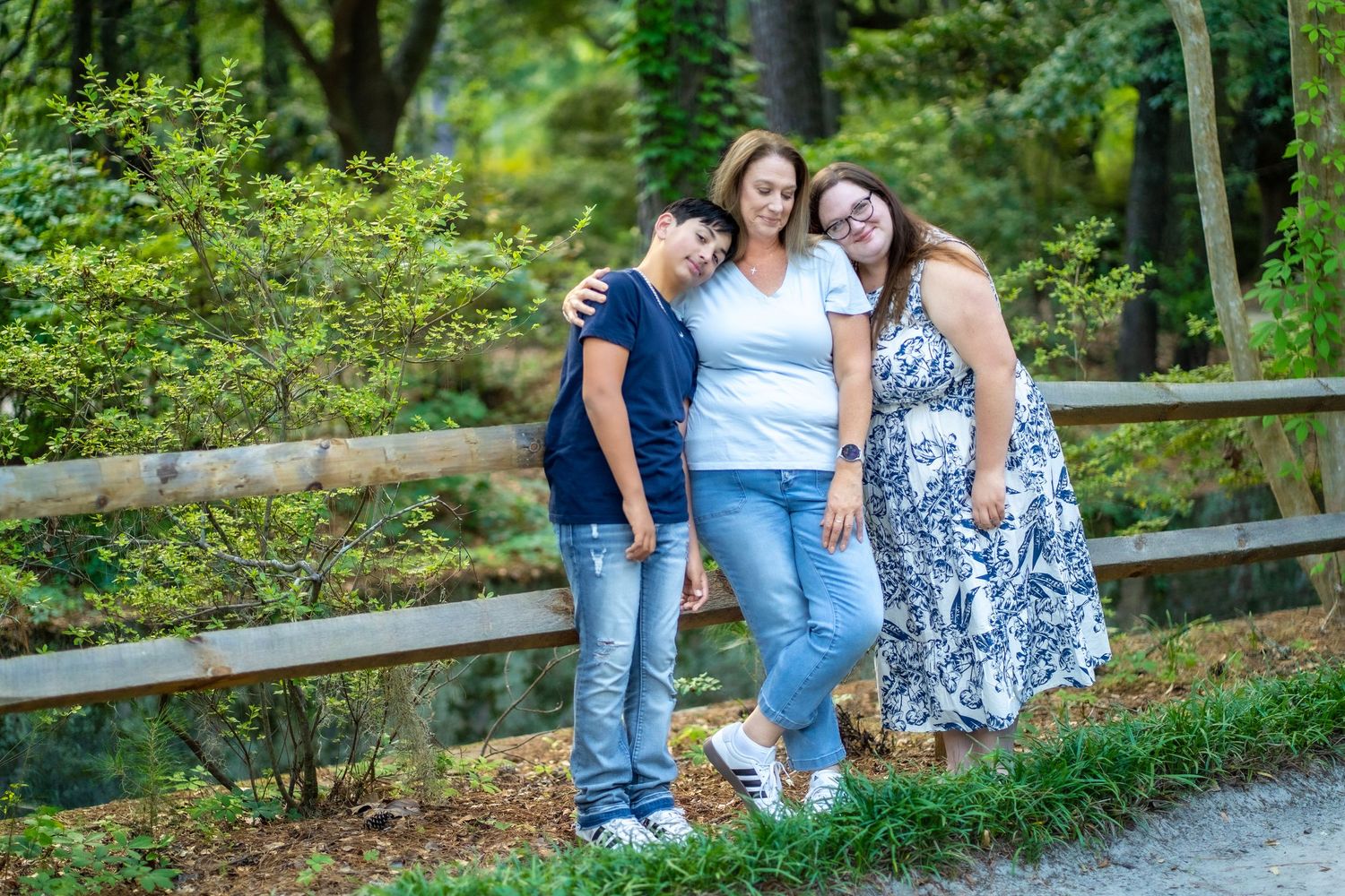 Three people pose together on forest path wearing casual summer outfits.