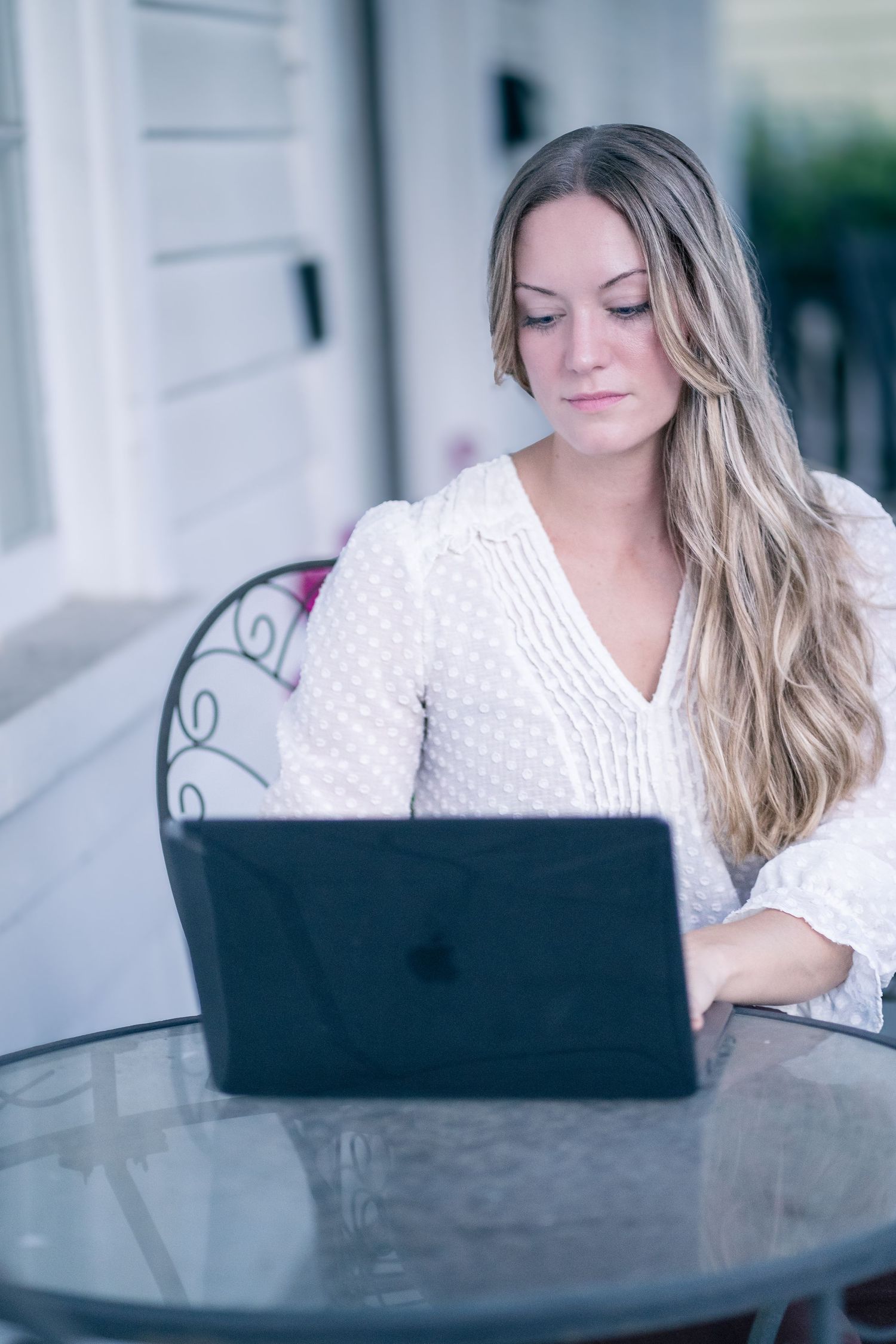 Professional working from home on laptop at outdoor table wearing white eyelet top with long blonde hair.