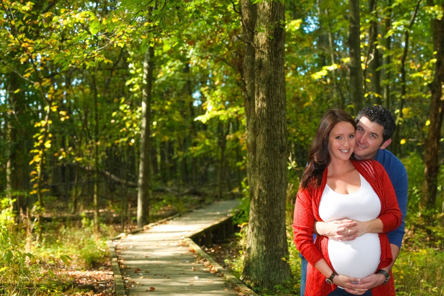 Romantic maternity photo of couple on wooden boardwalk surrounded by autumn forest.