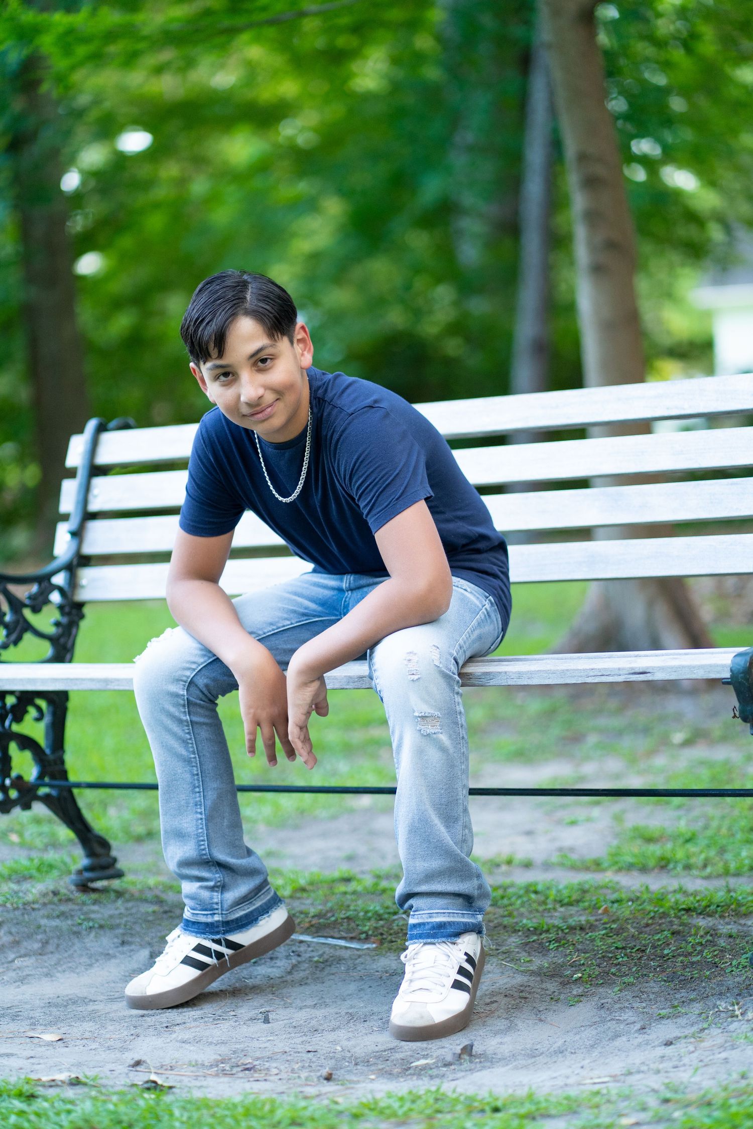Person in navy shirt and light jeans sitting on white park bench surrounded by greenery.