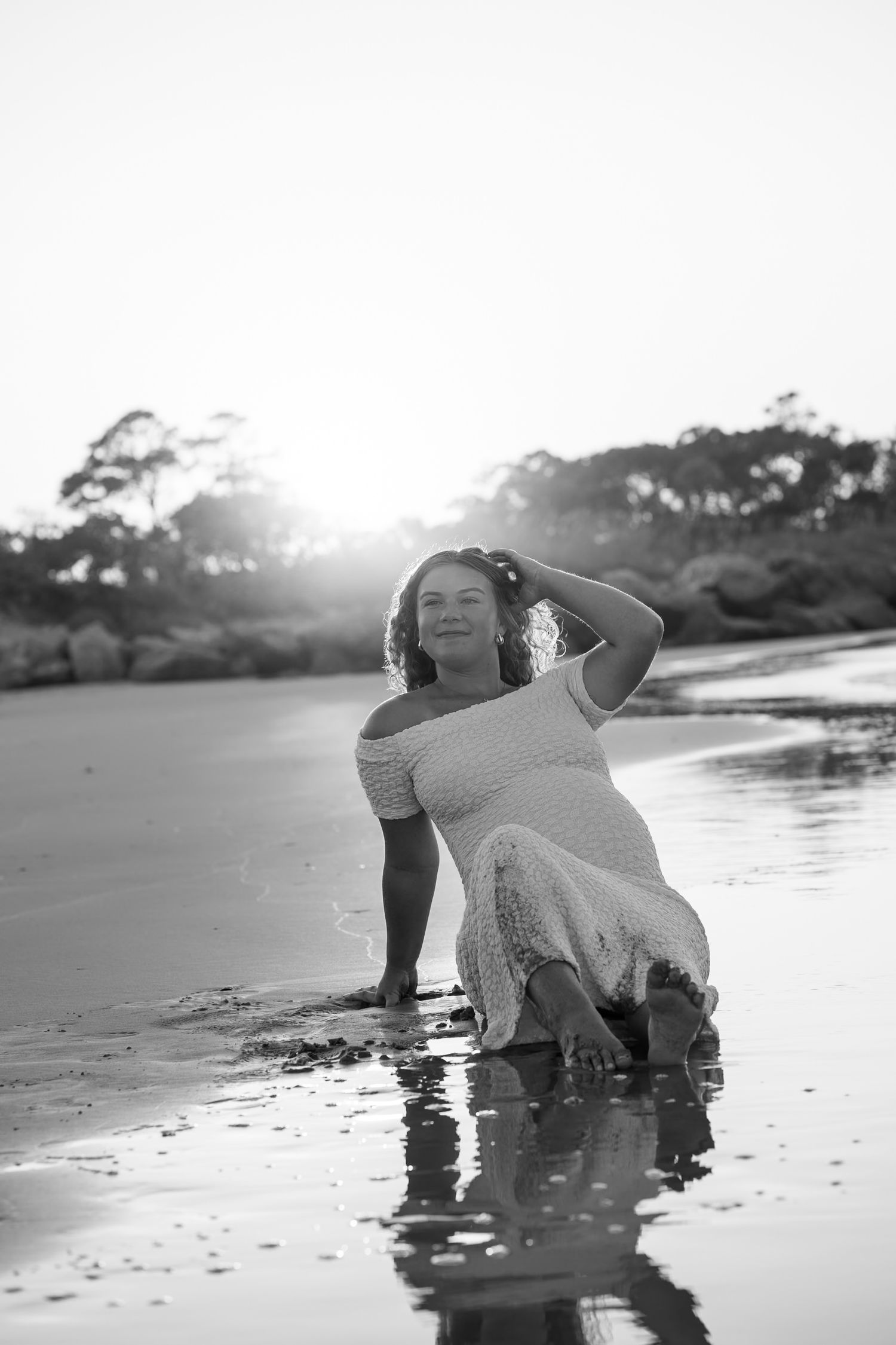Black and white photograph showing reflections in wet sand along a peaceful beach at sunset.