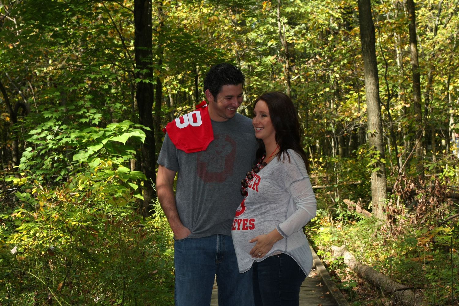 Couple in casual wear posing together in autumn forest setting.