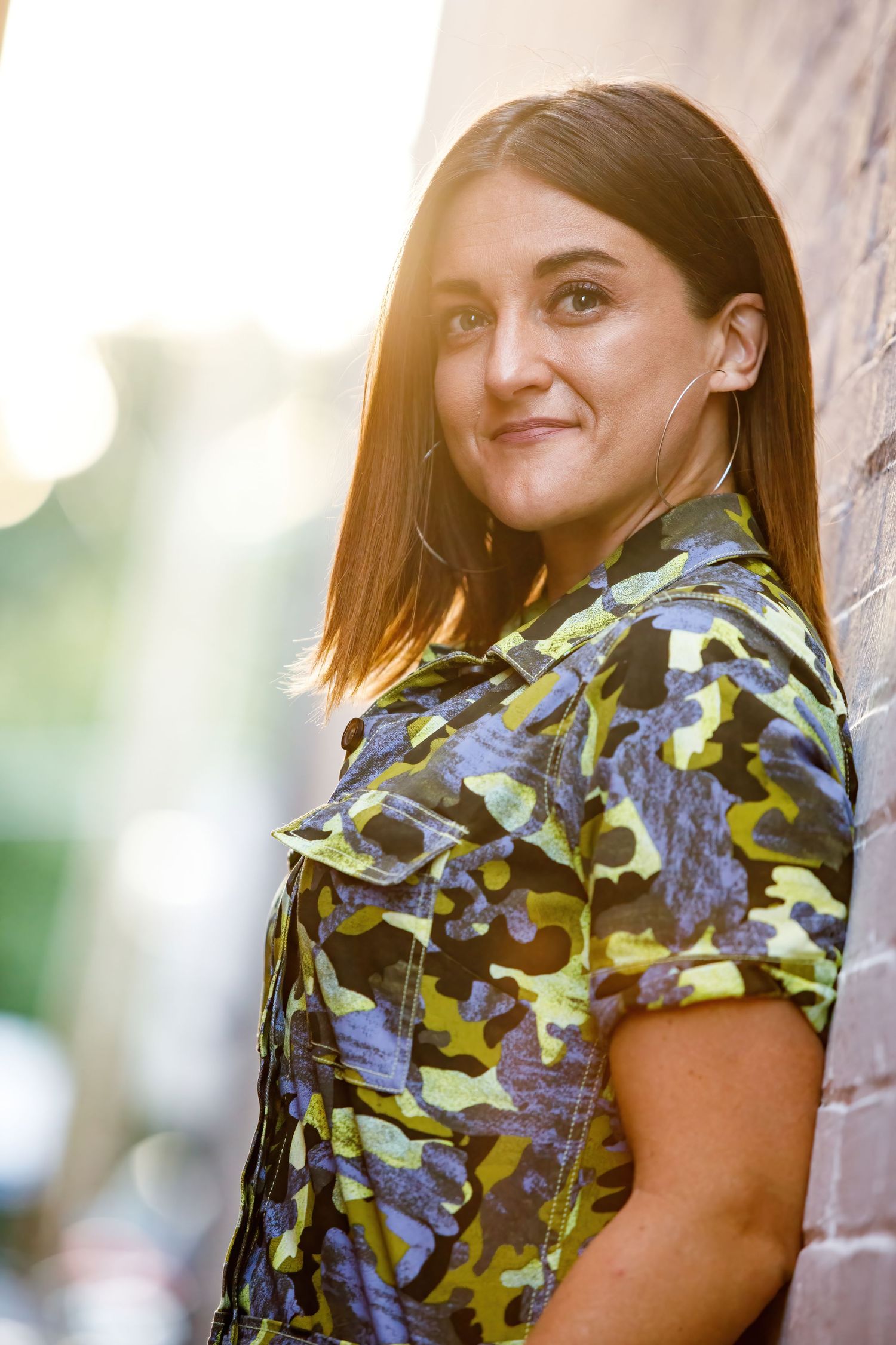 A person in a blue and yellow camouflage top poses against a wall in outdoor natural lighting.