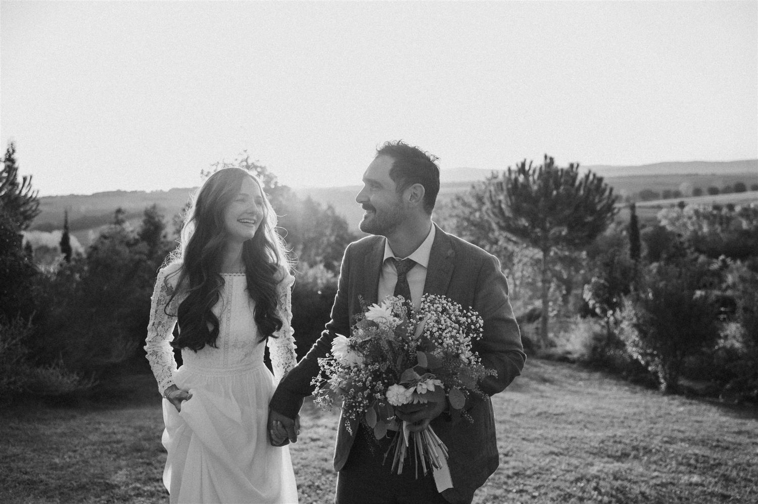 A black and white portrait of a couple laughing together with a floral bouquet.
