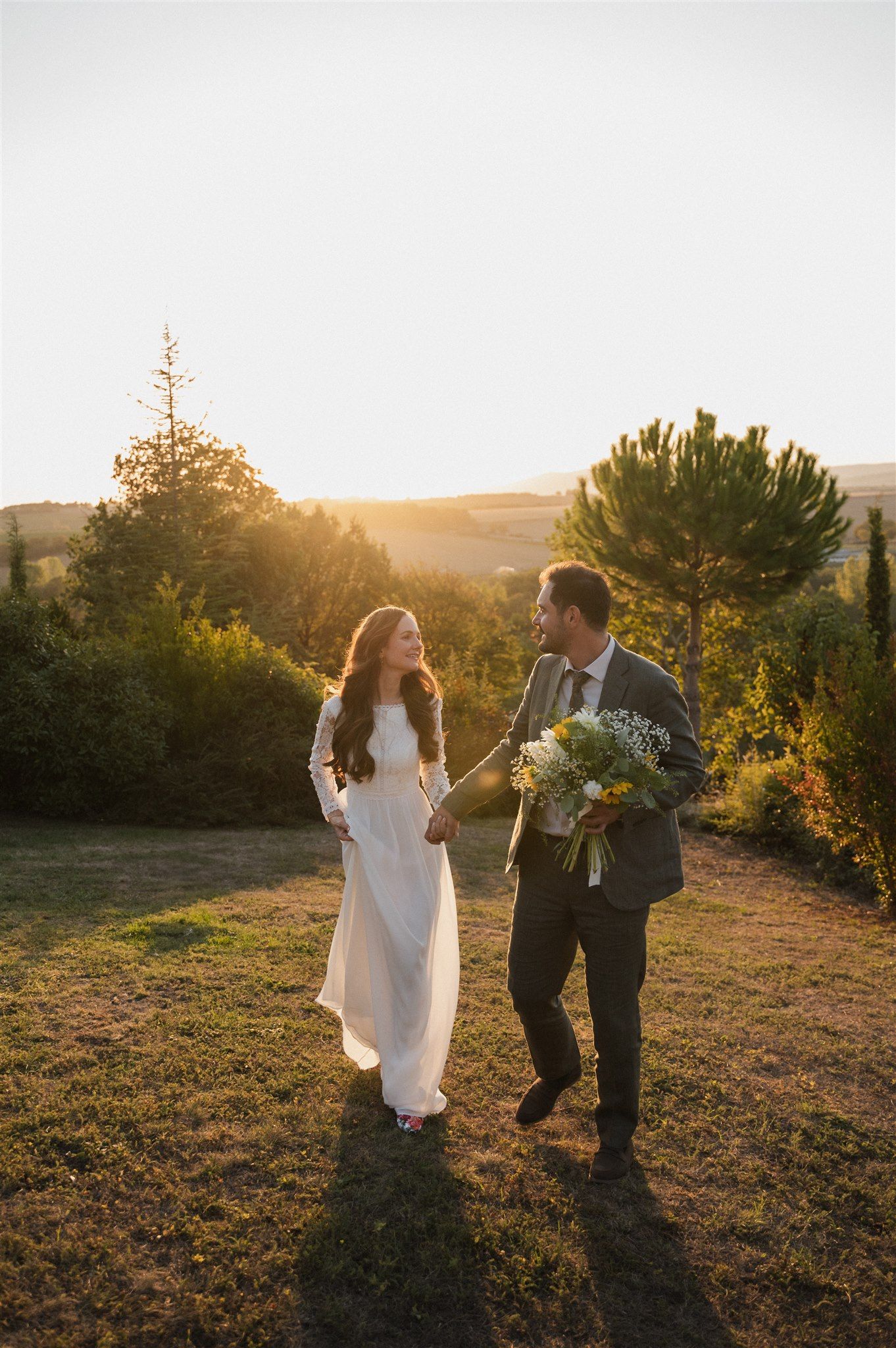 A couple dances playfully in a field at golden hour, surrounded by warm sunlight and nature.