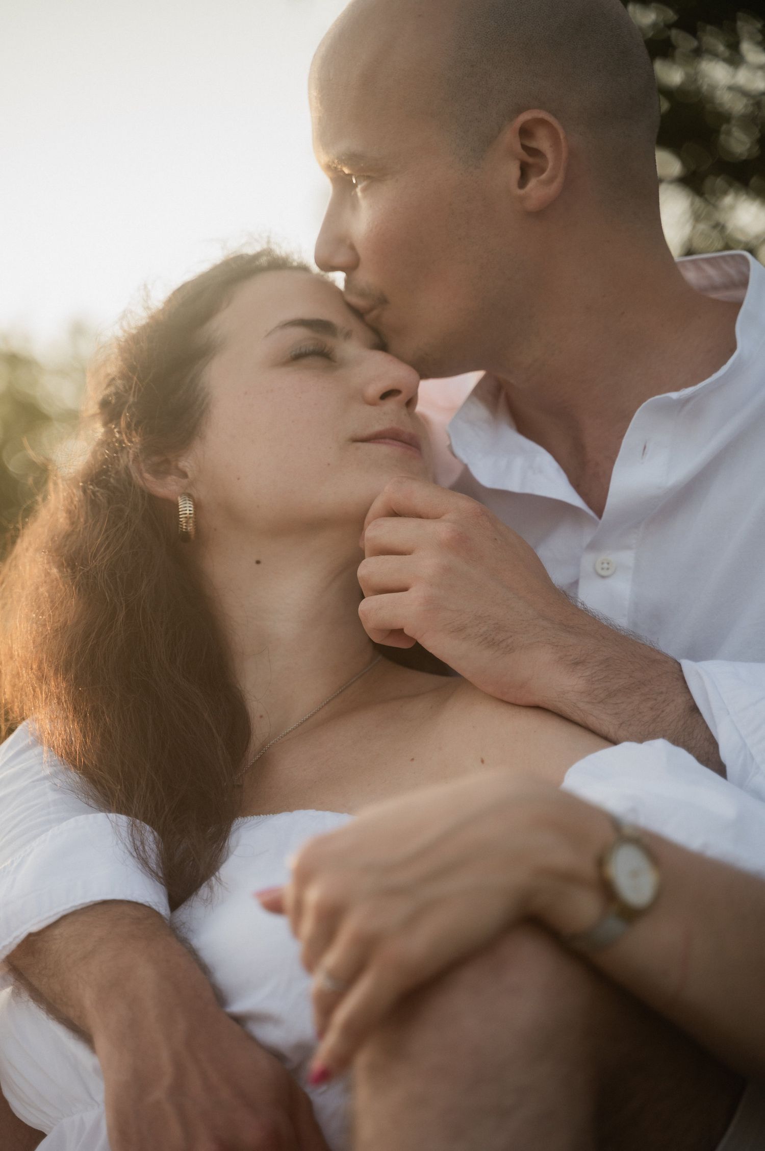 An intimate romantic moment between a couple wearing white as golden sunlight filters through the scene.