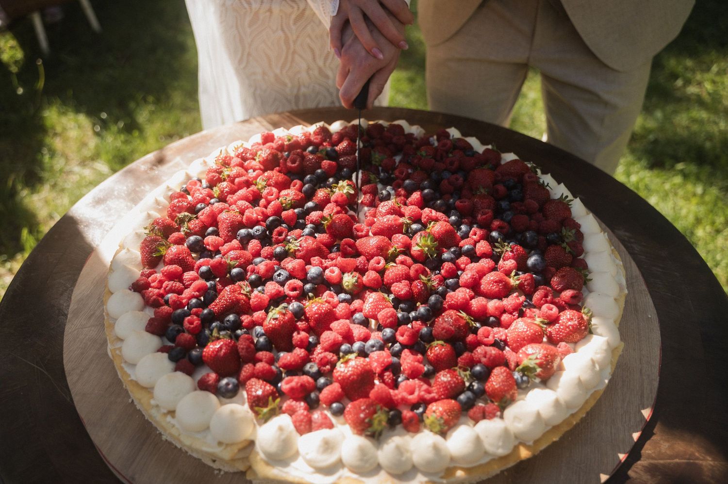 A homemade berry pie topped with fresh raspberries and blueberries on a whipped cream base in an outdoor setting.