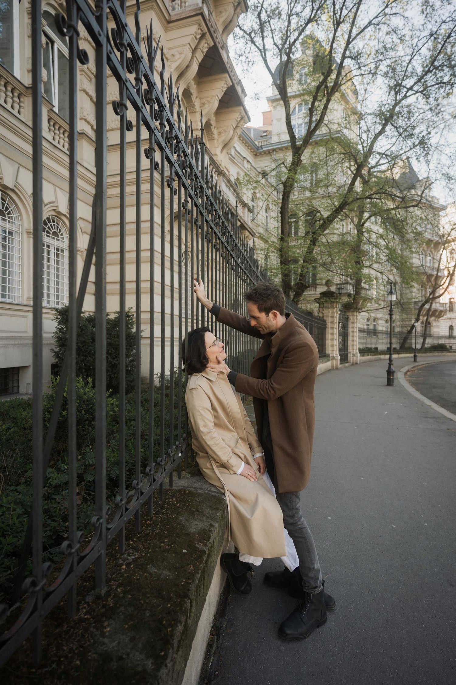 A couple shares a romantic moment along an elegant covered walkway with arched columns and iron railings.