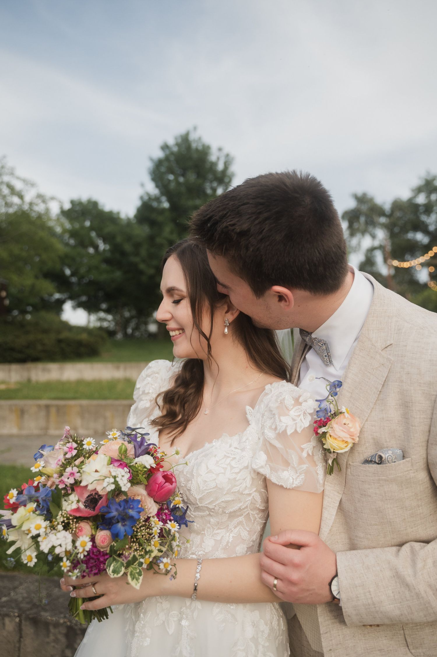 Newlyweds sharing intimate moment with colorful bouquet in outdoor garden setting.