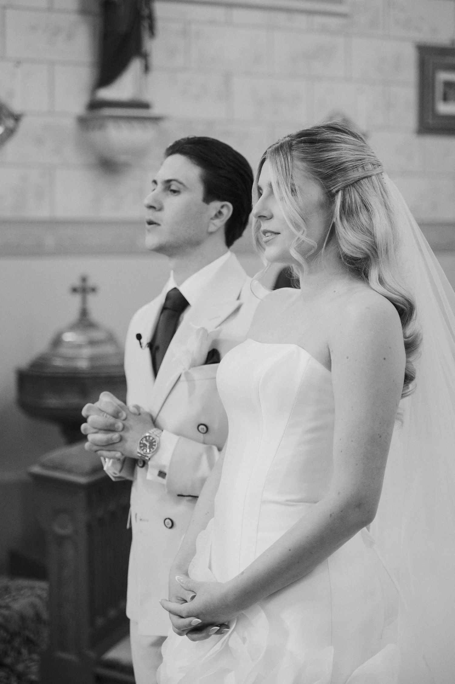 Bride and groom standing at church altar during wedding ceremony in elegant black and white portrait.