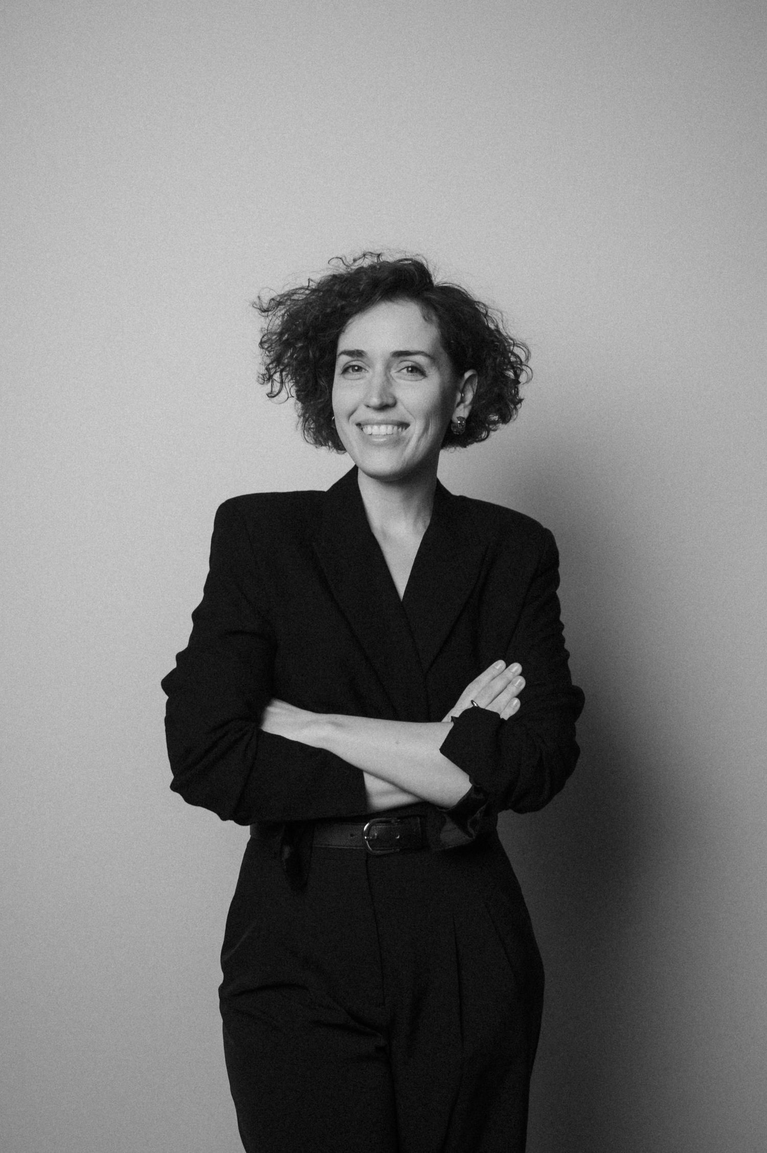 A black and white photo series showing someone posing in a dark blazer against a light background.