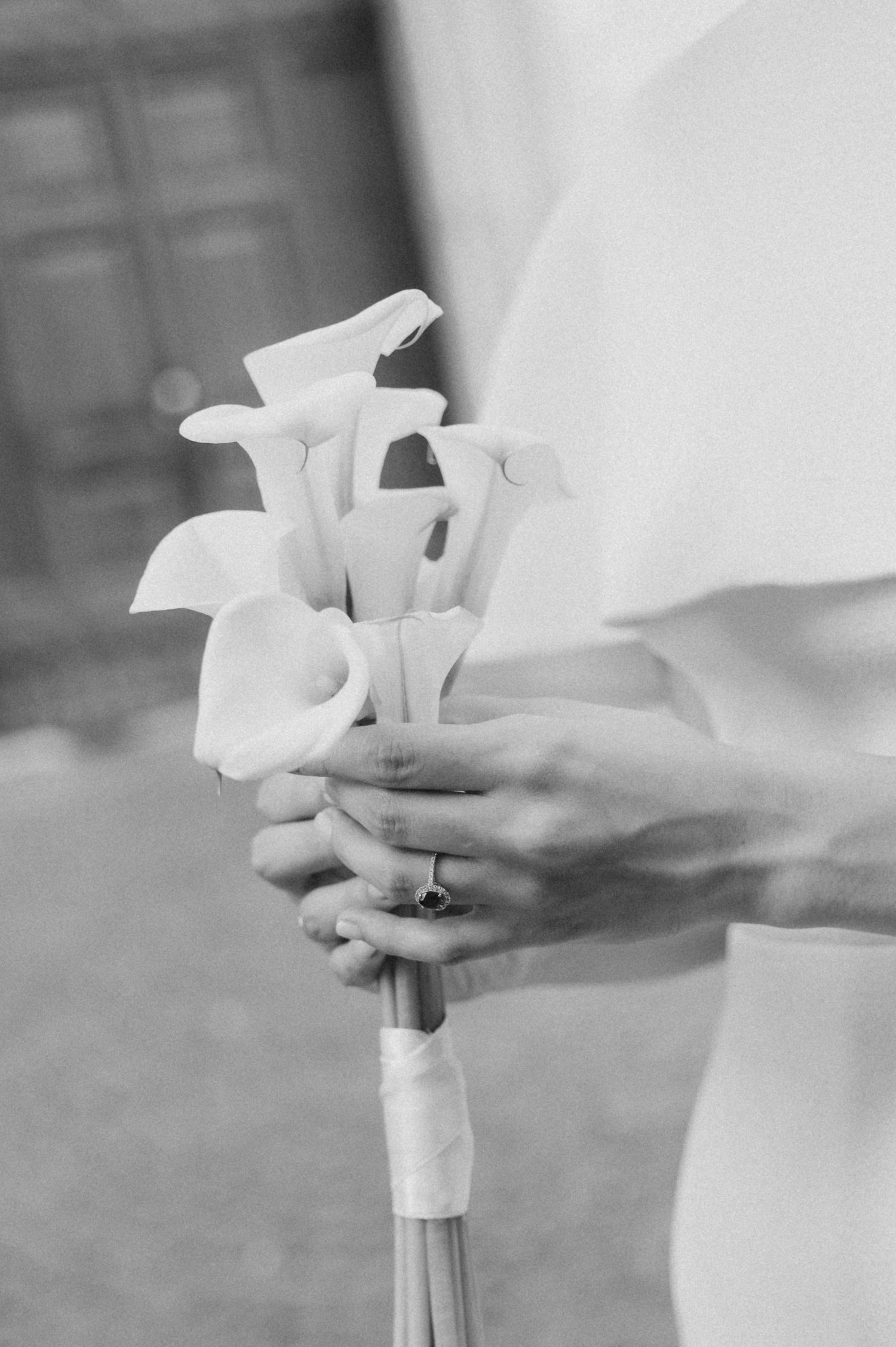 Monochrome close-up of hands holding a classic white calla lily bouquet.