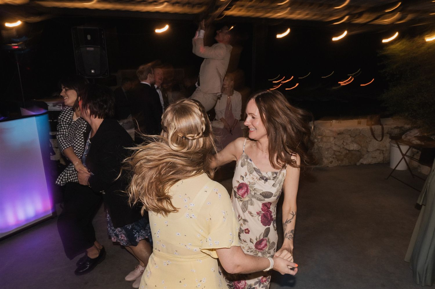Wedding reception dance floor filled with guests enjoying the celebration under dim lighting.