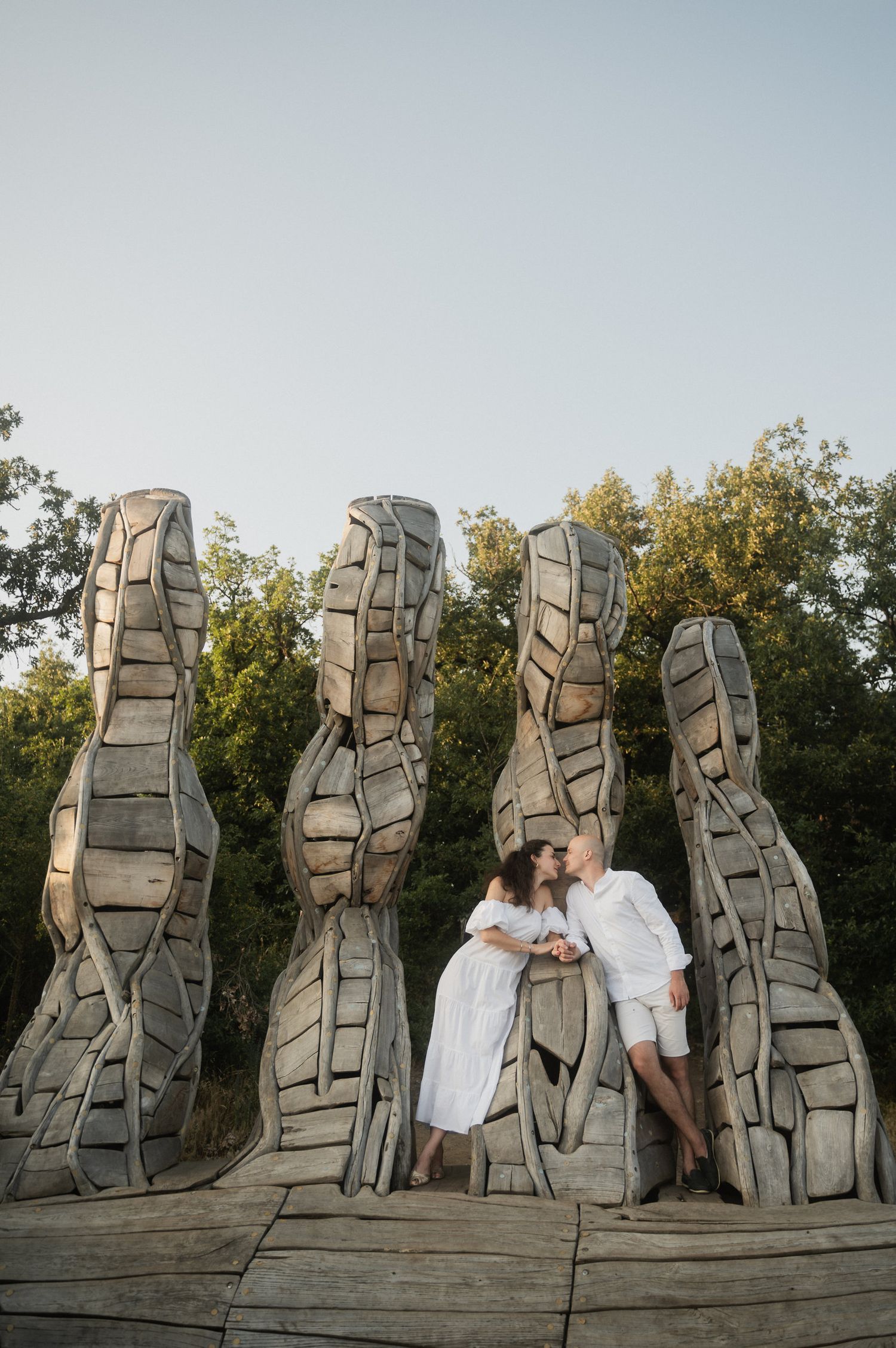 A couple shares a romantic moment in front of tall stone sculptures in an outdoor setting at sunset.
