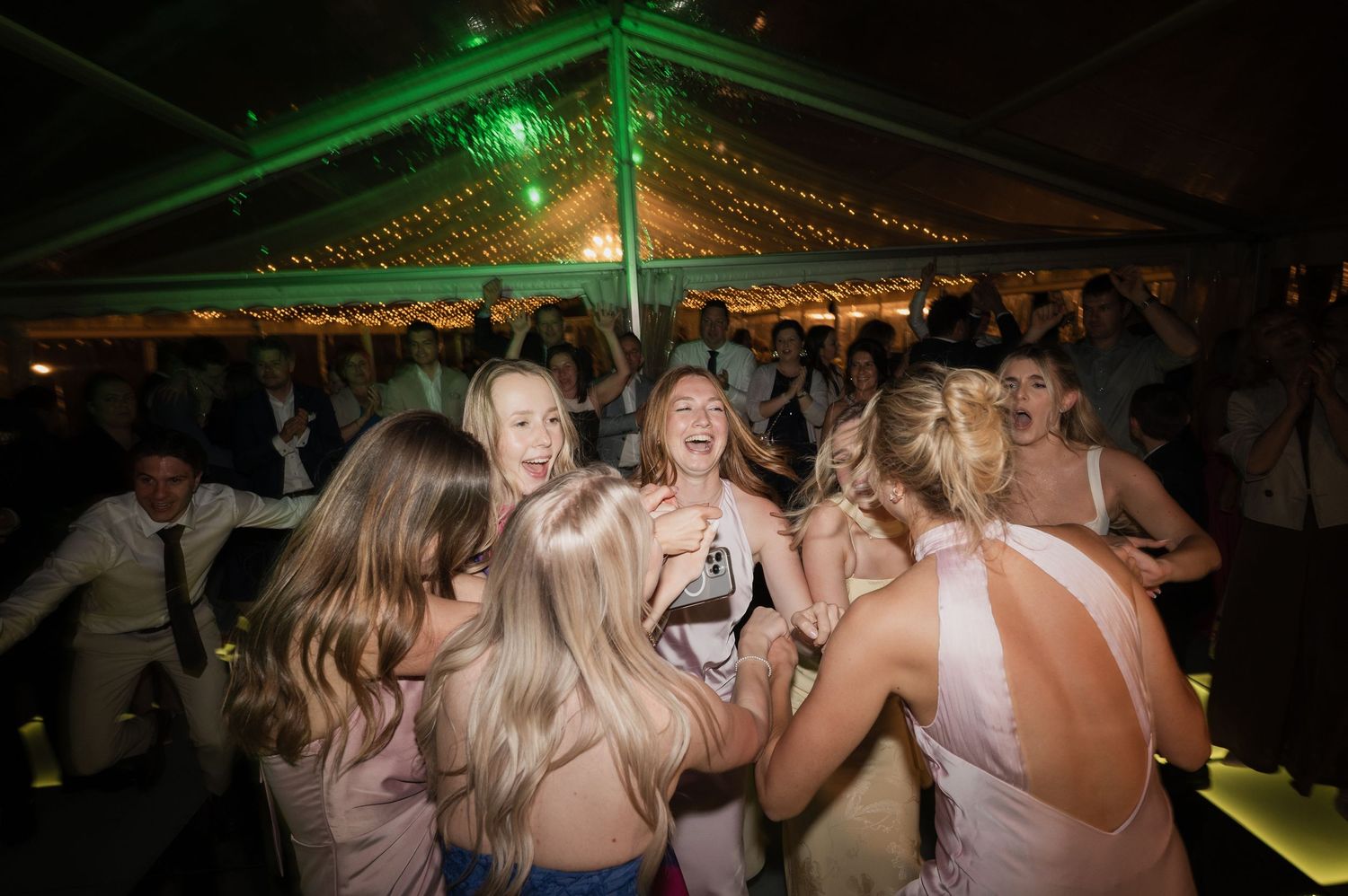 Bridesmaids in pink dresses dancing and celebrating joyfully at a wedding reception under a tent.