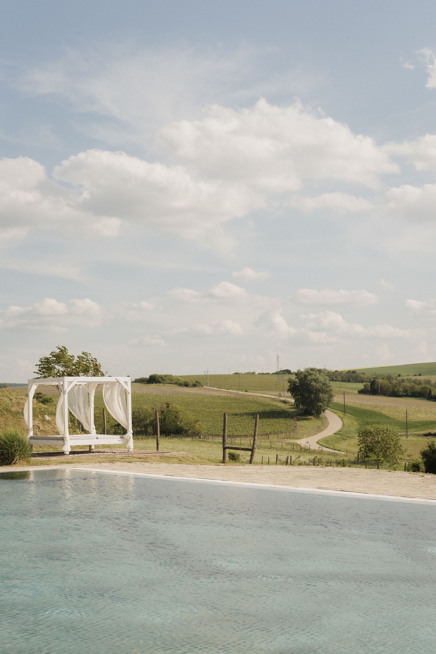 Serene infinity pool overlooking rolling green countryside with white canopy gazebo under cloudy sky.