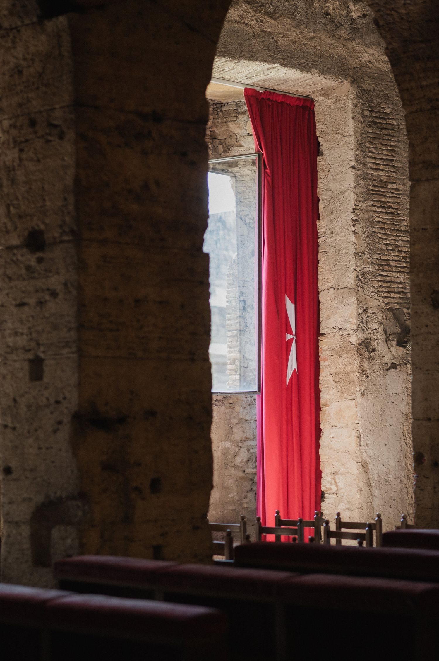 Interior view of historic brick building with red curtains and dramatic lighting through arched windows.