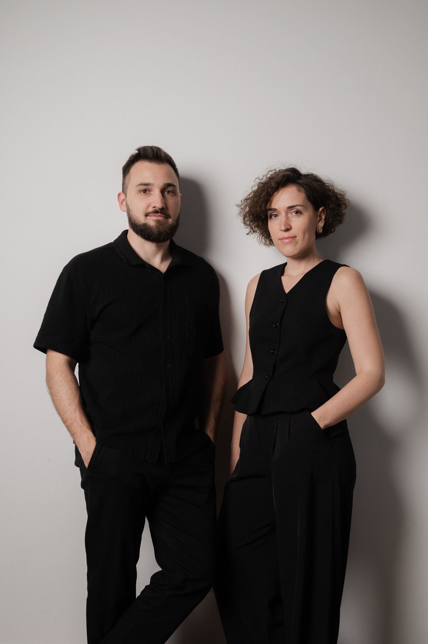 A couple in black outfits poses together against a gray wall in a series of artistic portrait photos.