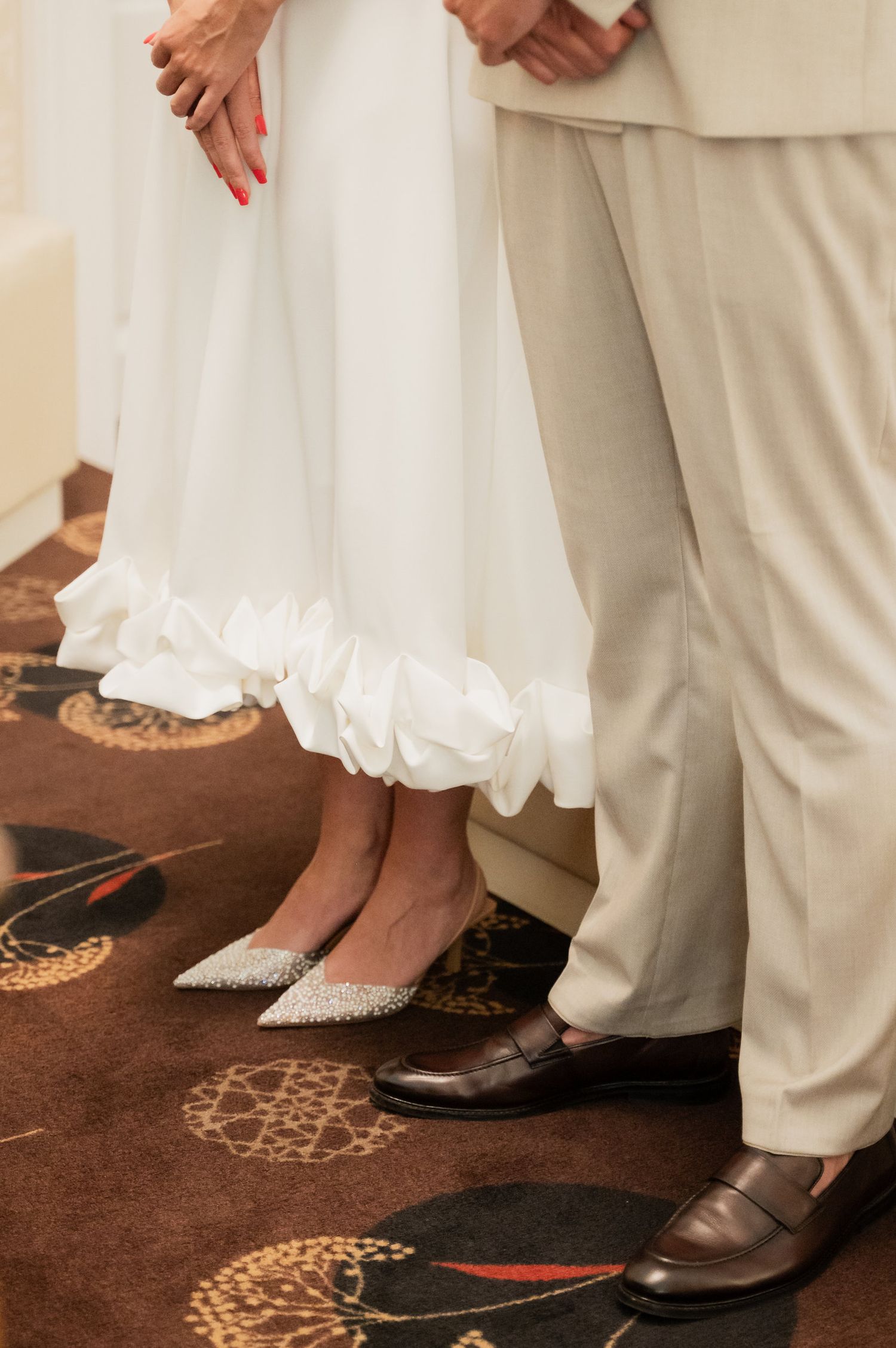 Wedding shoes and dress details shown against a patterned carpet floor.