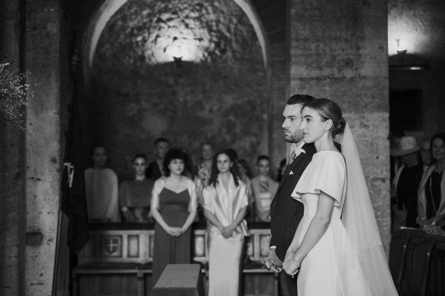 Wedding ceremony progression shown in black and white photographs within a stone church setting.