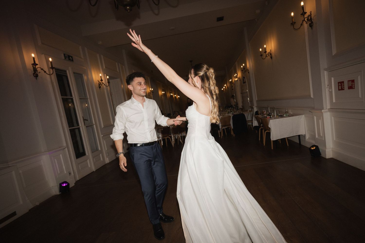 Bride and groom share their first dance in an elegant ballroom, with the bride raising her arm gracefully.