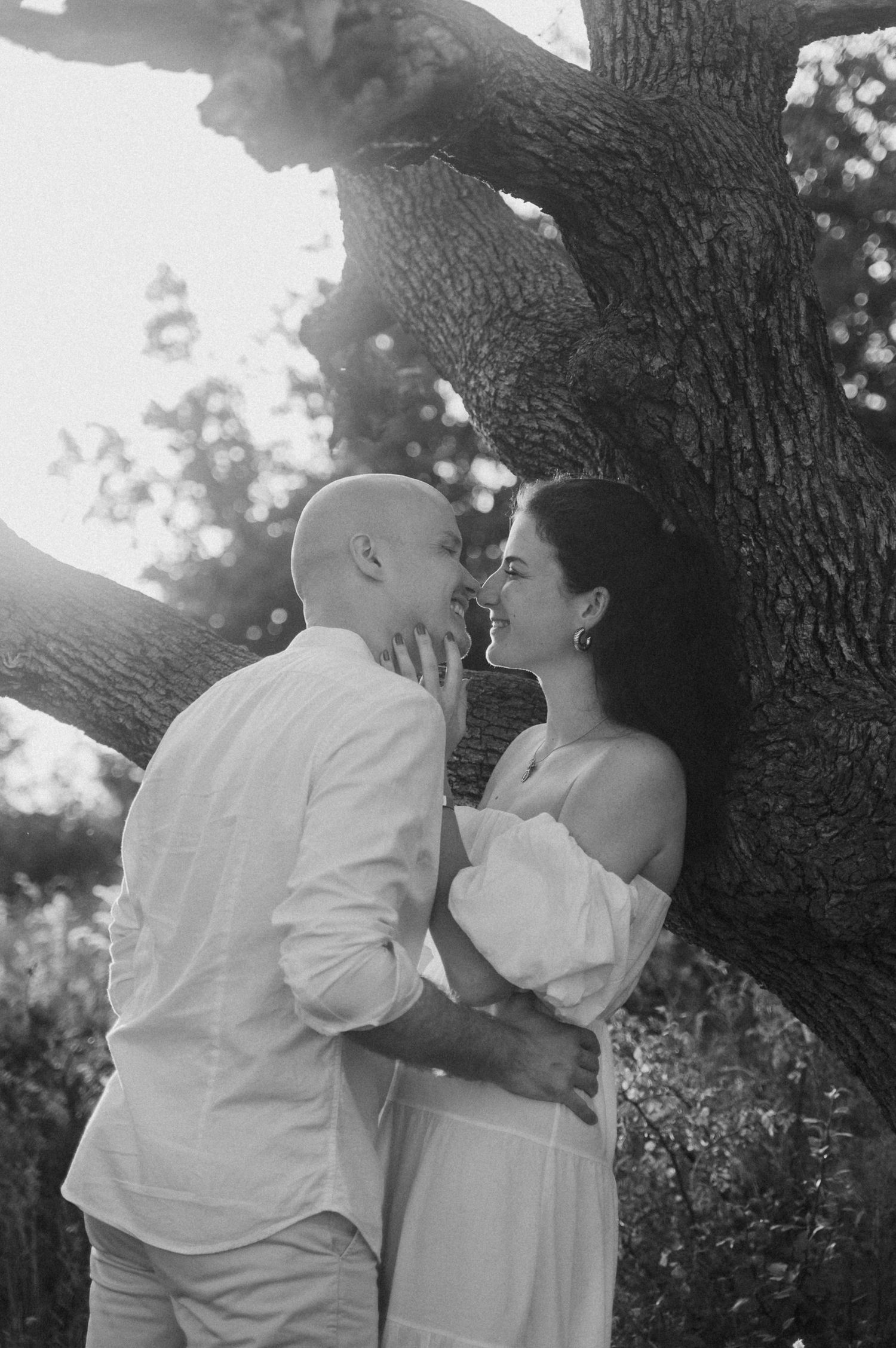 A romantic black and white photo sequence of a couple sharing tender moments against a tree trunk in nature.