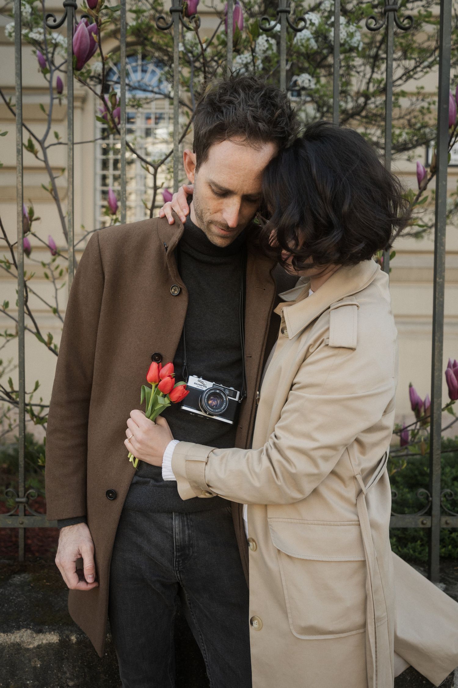 A couple in casual attire sharing an intimate moment outdoors against a garden backdrop.