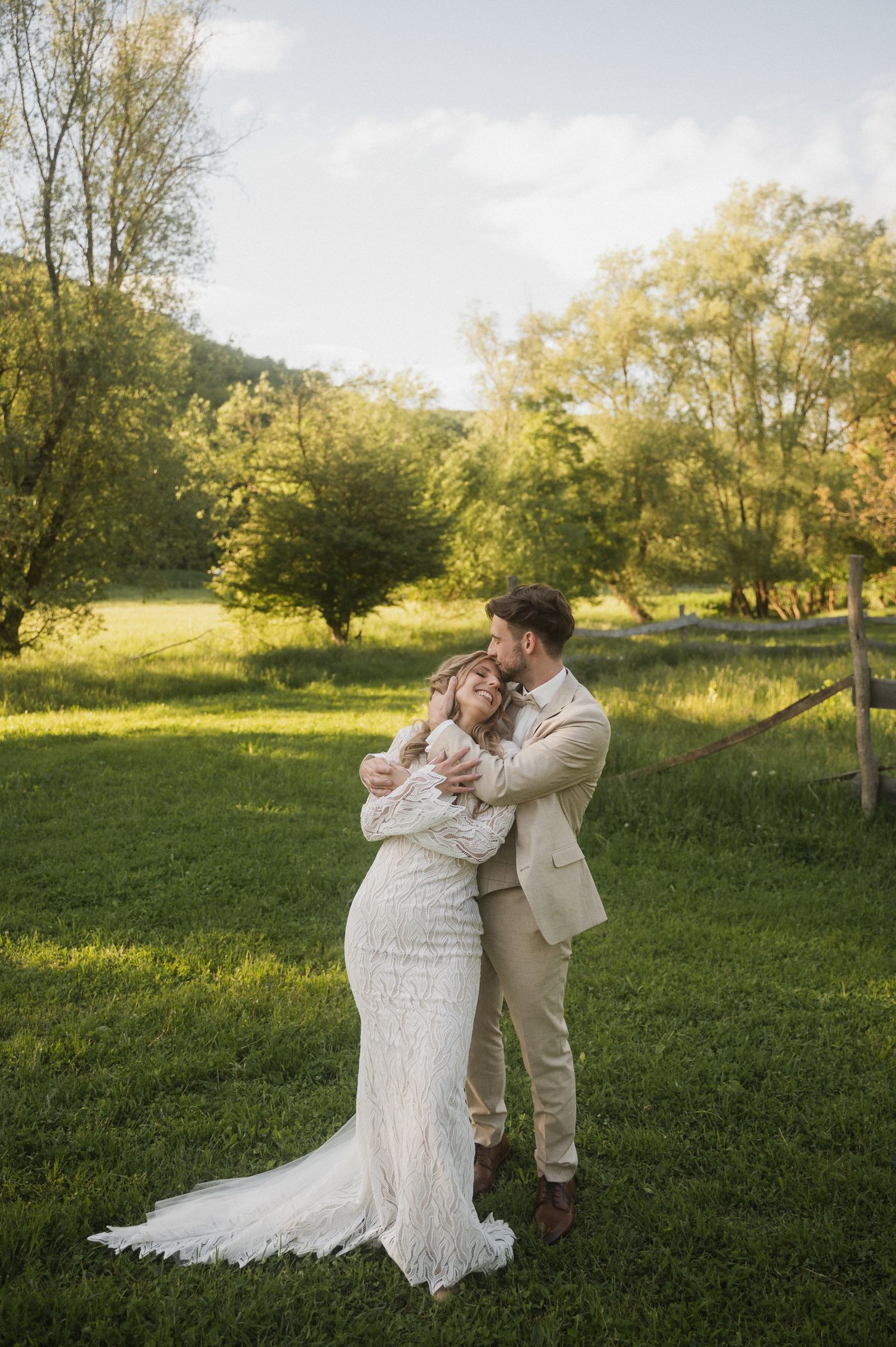 A couple dances together in a romantic dip pose on a grassy field during golden hour with trees in the background.