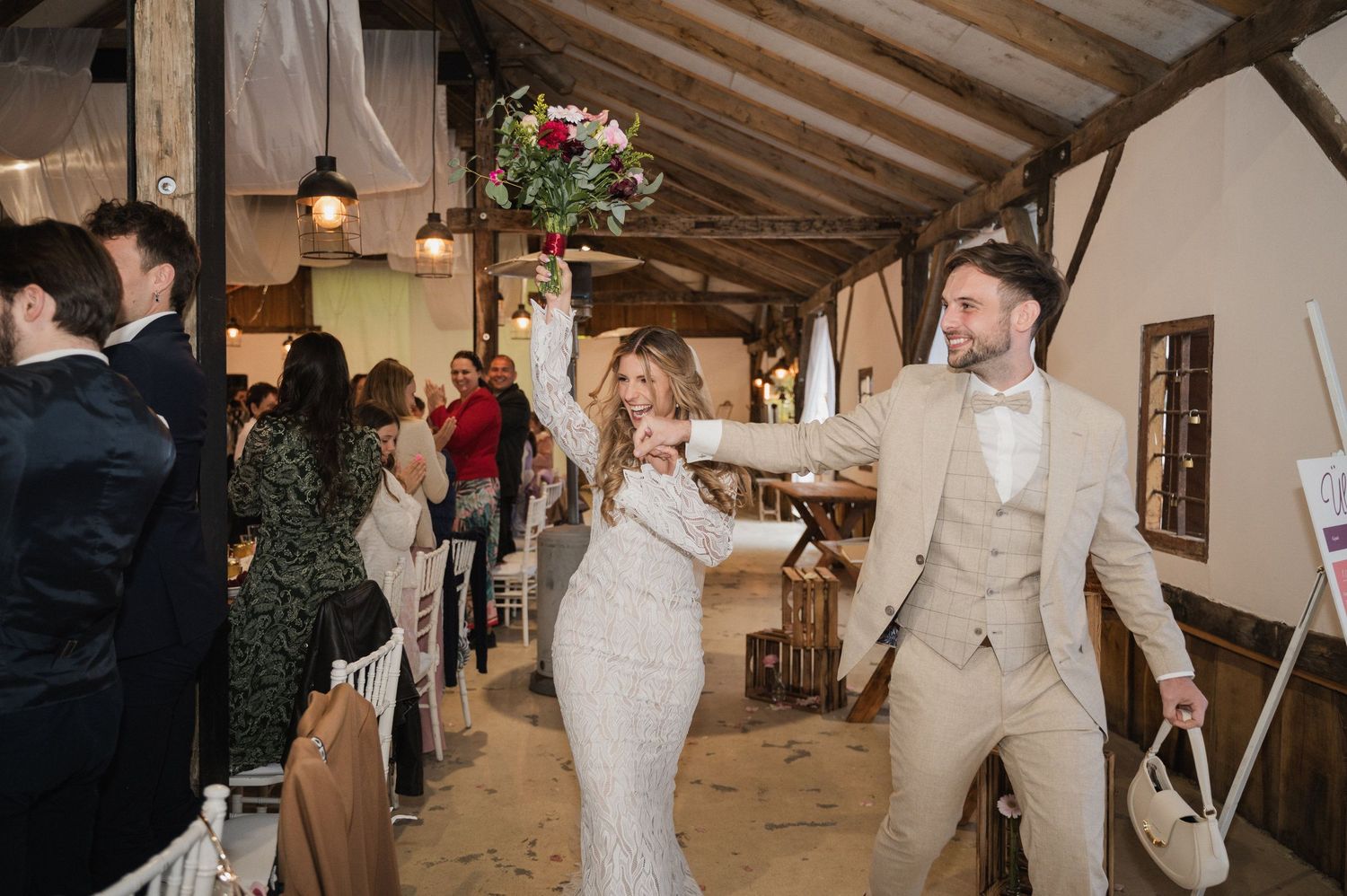 A couple dances together in an elegant rustic venue with exposed wooden beams and warm lighting.